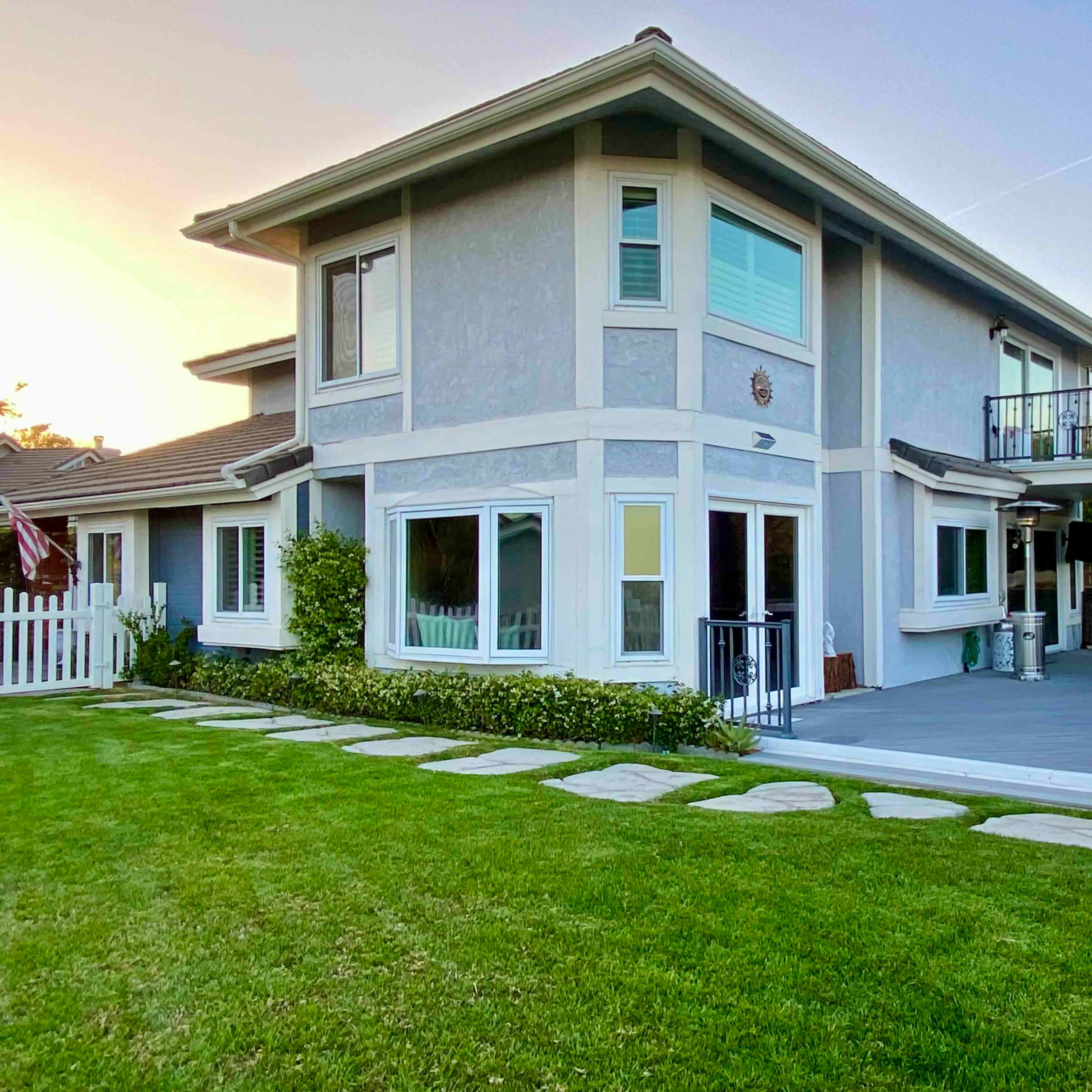 A modern two-story house features large windows and a deck overlooking a landscaped yard with a stone path.
