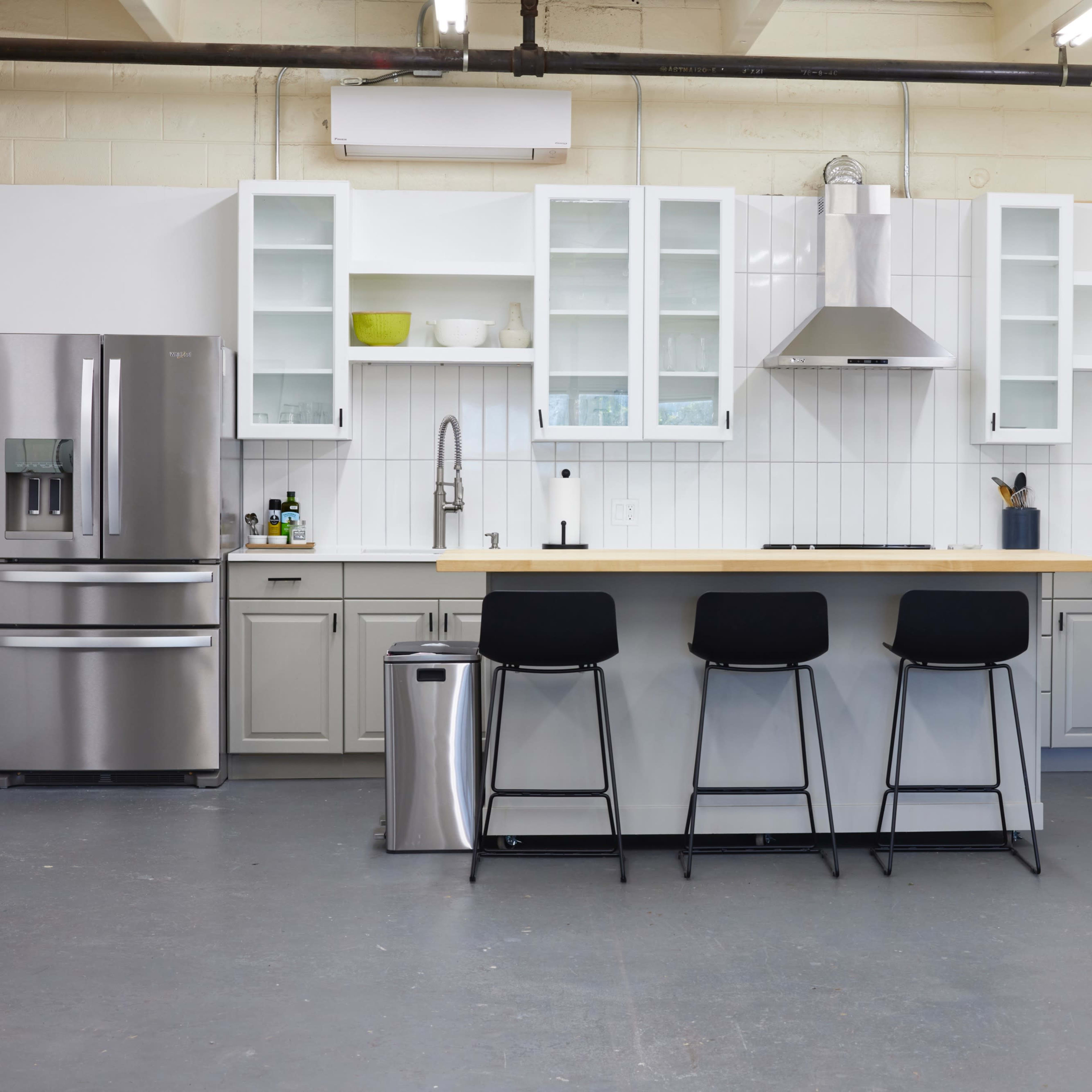 A modern kitchen features gray cabinetry, stainless steel appliances, a central island with bar stools, and open shelves displaying dishware.