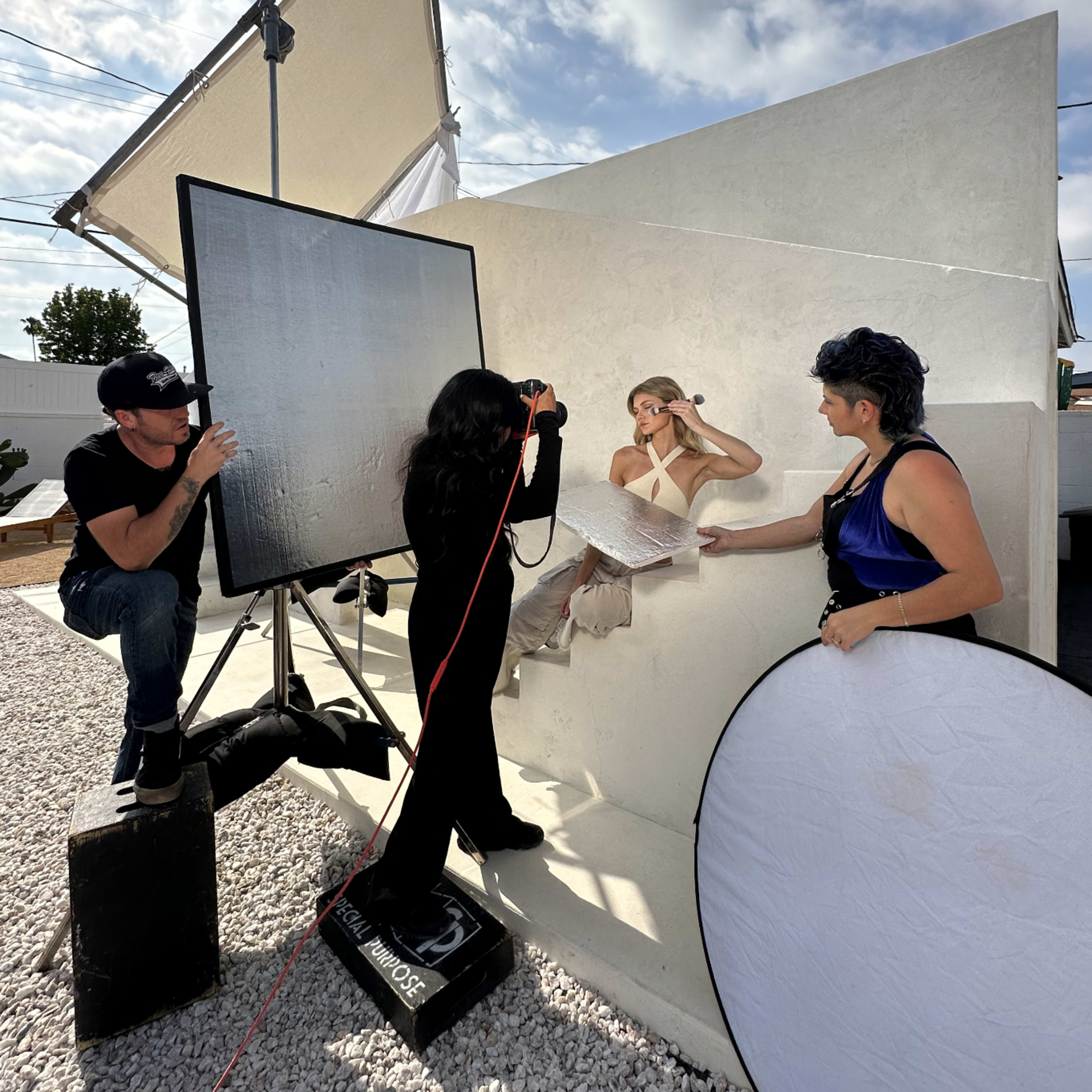 A photoshoot is taking place outdoors with a model on stairs and a team using lighting equipment and reflectors.