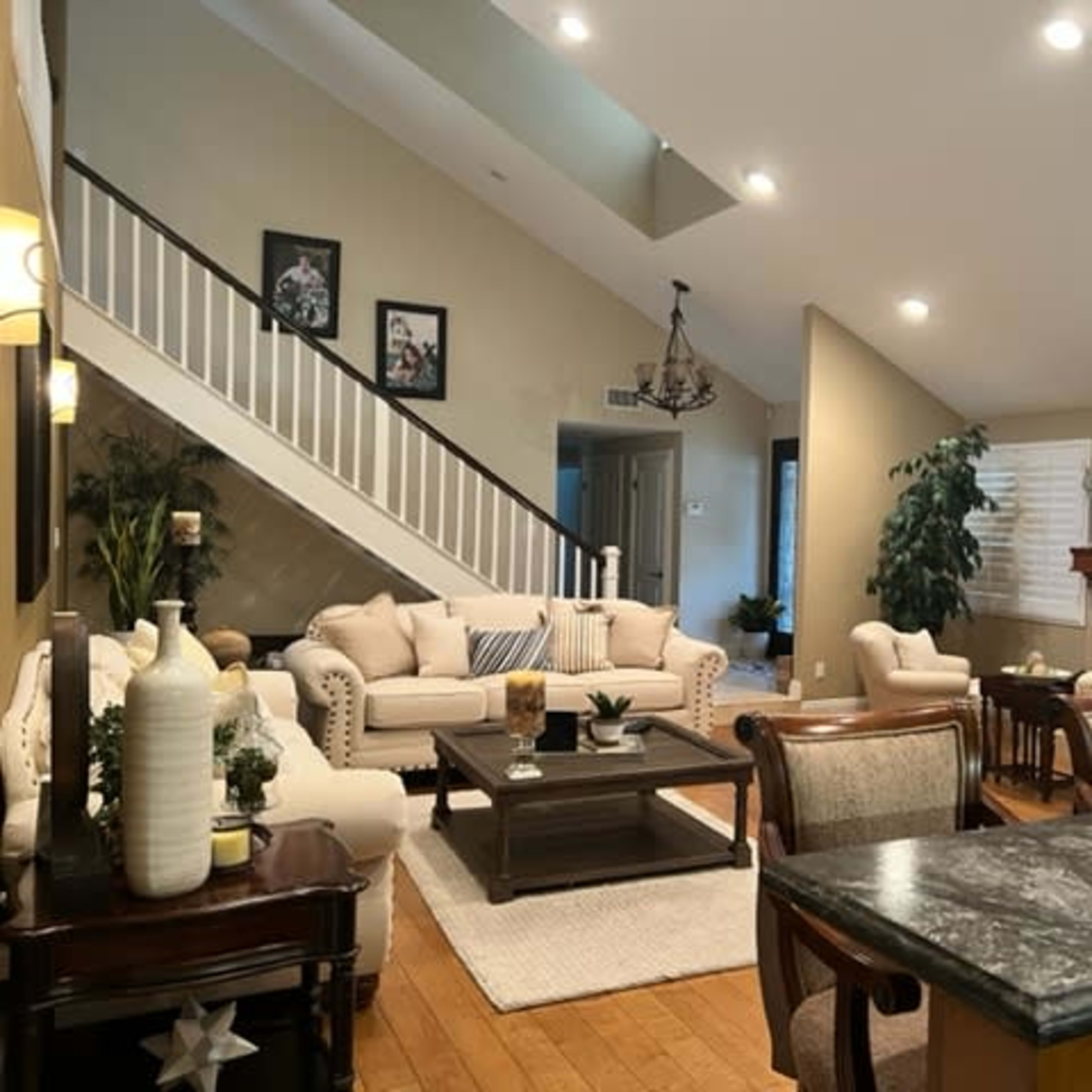 A spacious living area with a staircase, a light-colored sofa set, a wooden dining table, and a fireplace.