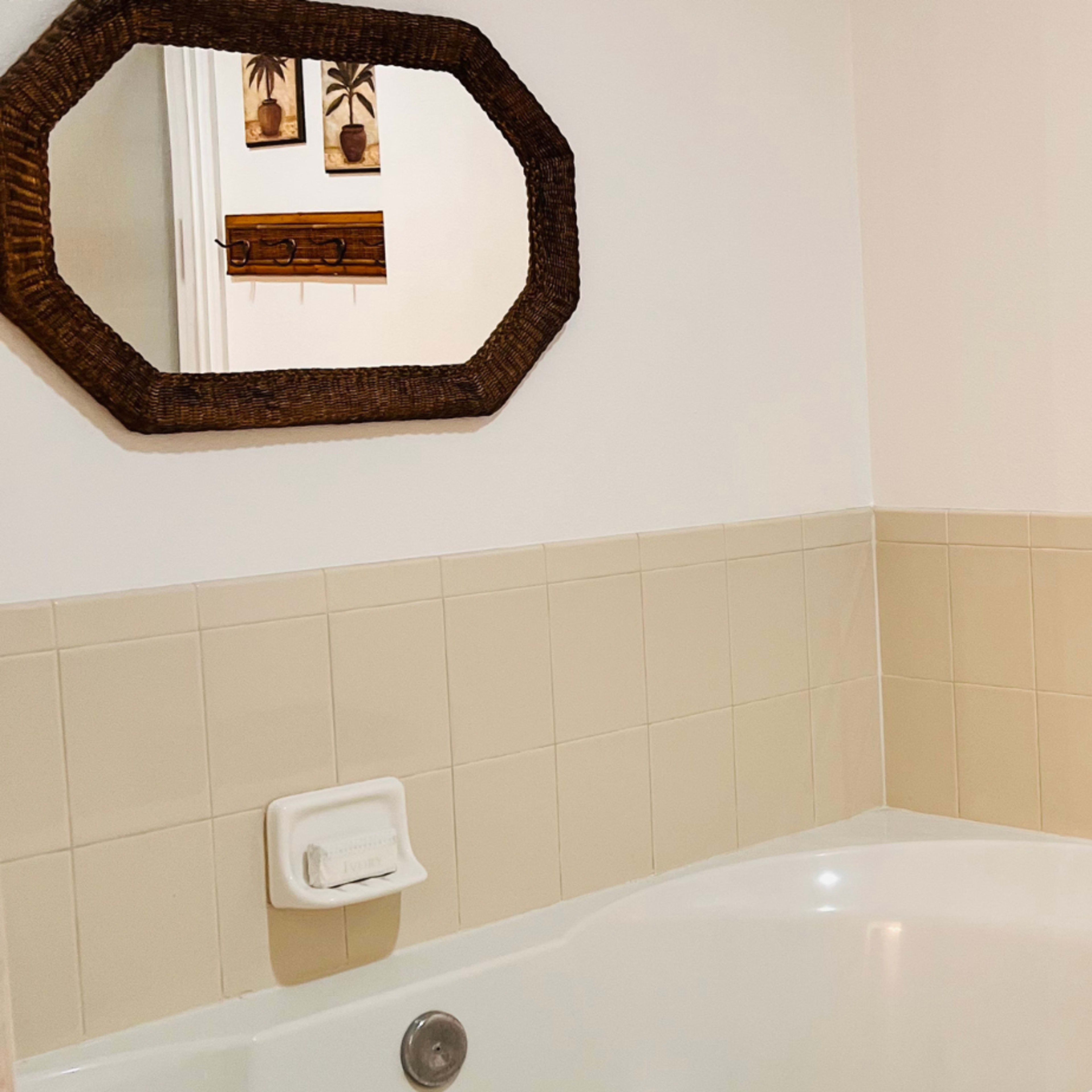 A bathroom with a white bathtub, beige tiled walls, and a rectangular mirror above the tub.