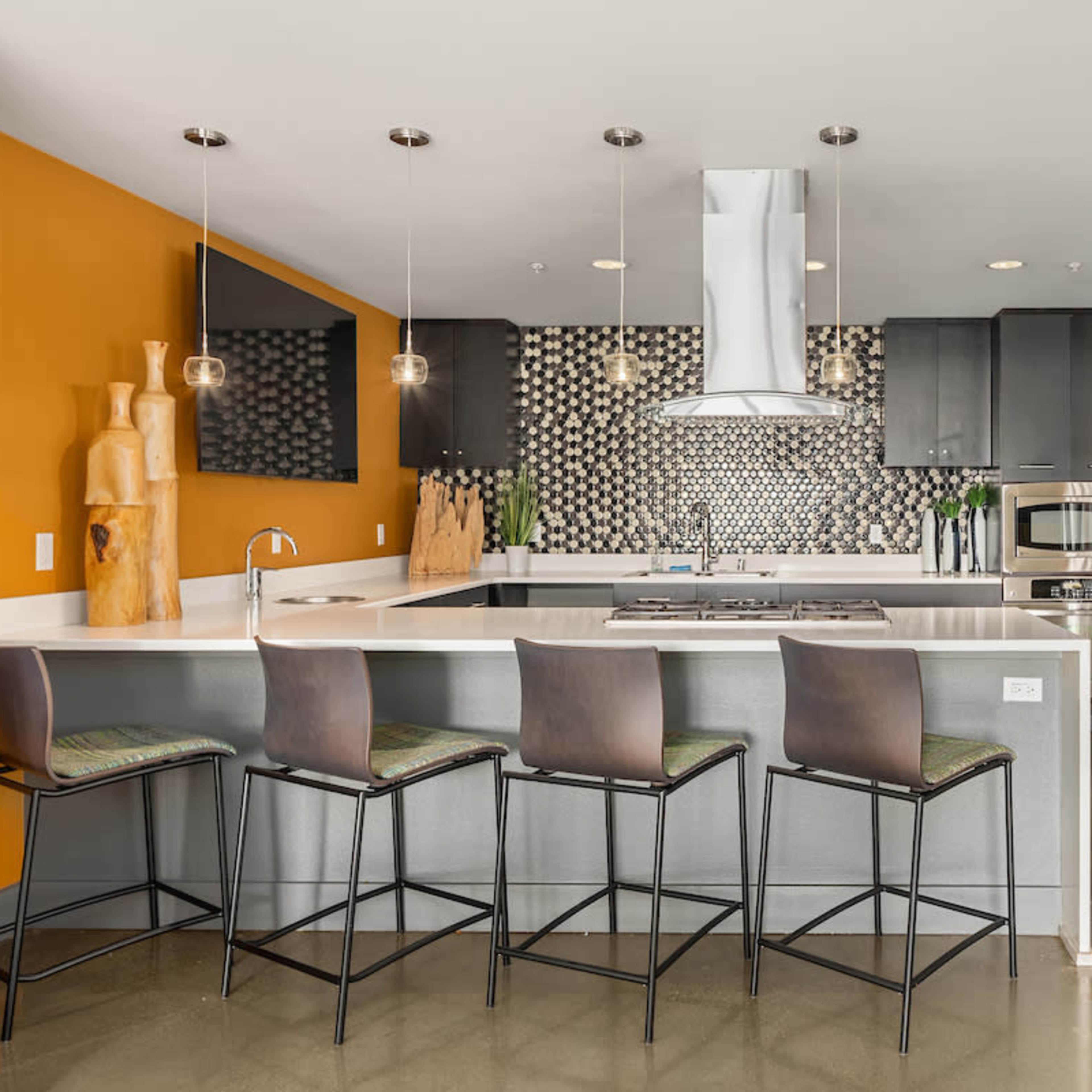 A modern kitchen featuring a sleek island with bar stools, dark cabinets, a stainless steel refrigerator, and a striking patterned backsplash.