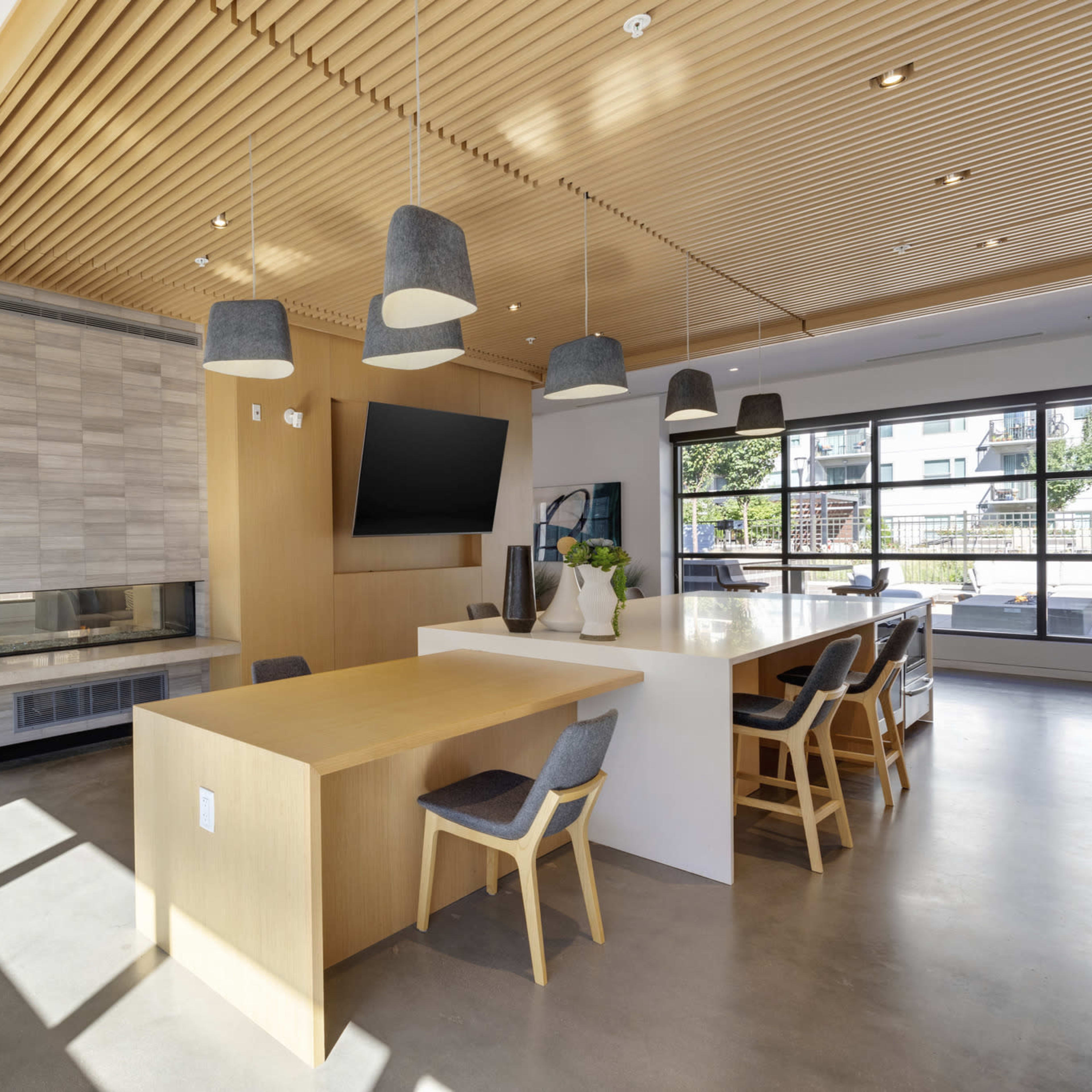 A modern interior space featuring a kitchen island, dining area, and a large window with natural light, highlighted by wooden ceiling panels and minimalist decor.
