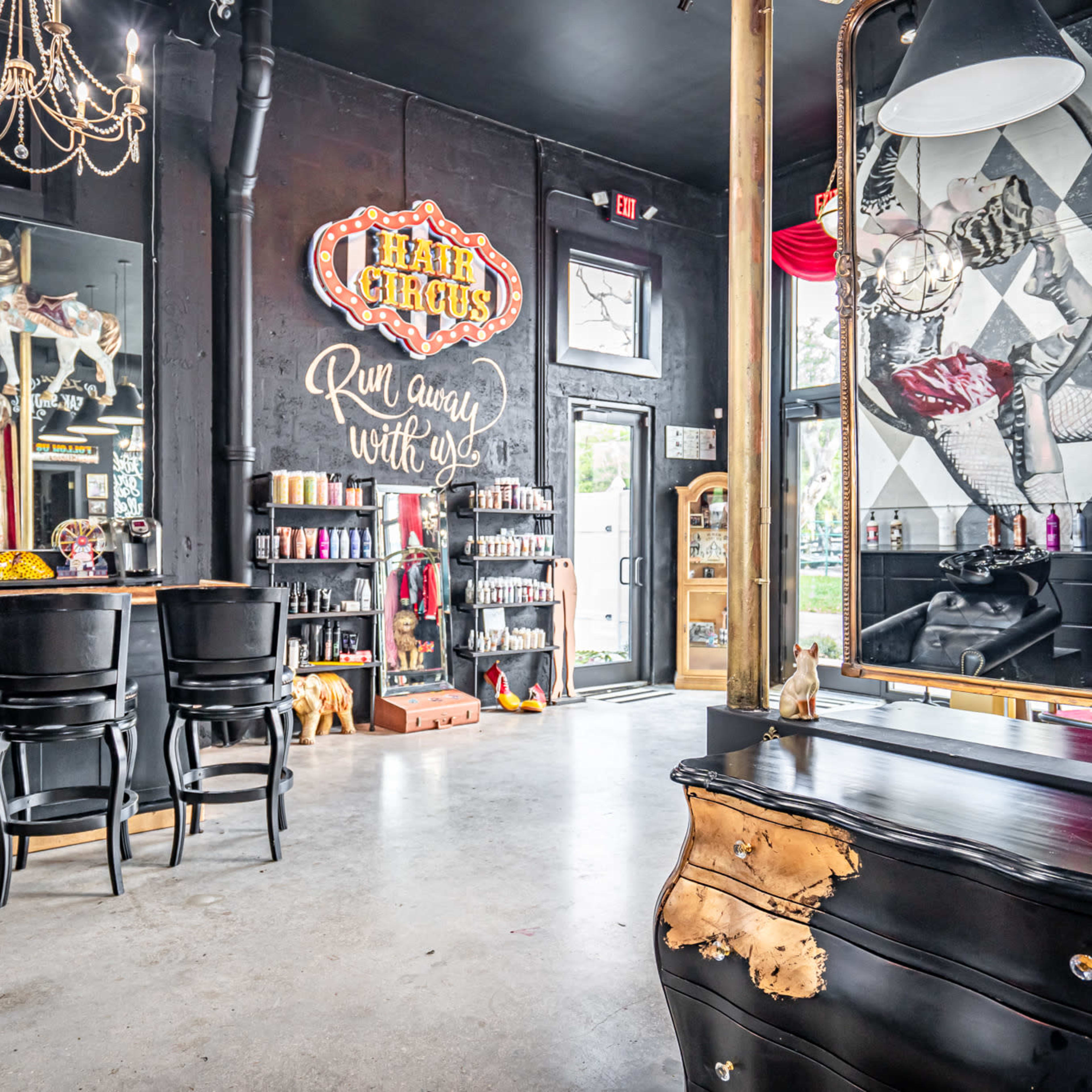 A stylish salon interior featuring a bar counter, a large mirror, and decorative elements like a chandelier and a vintage sign.