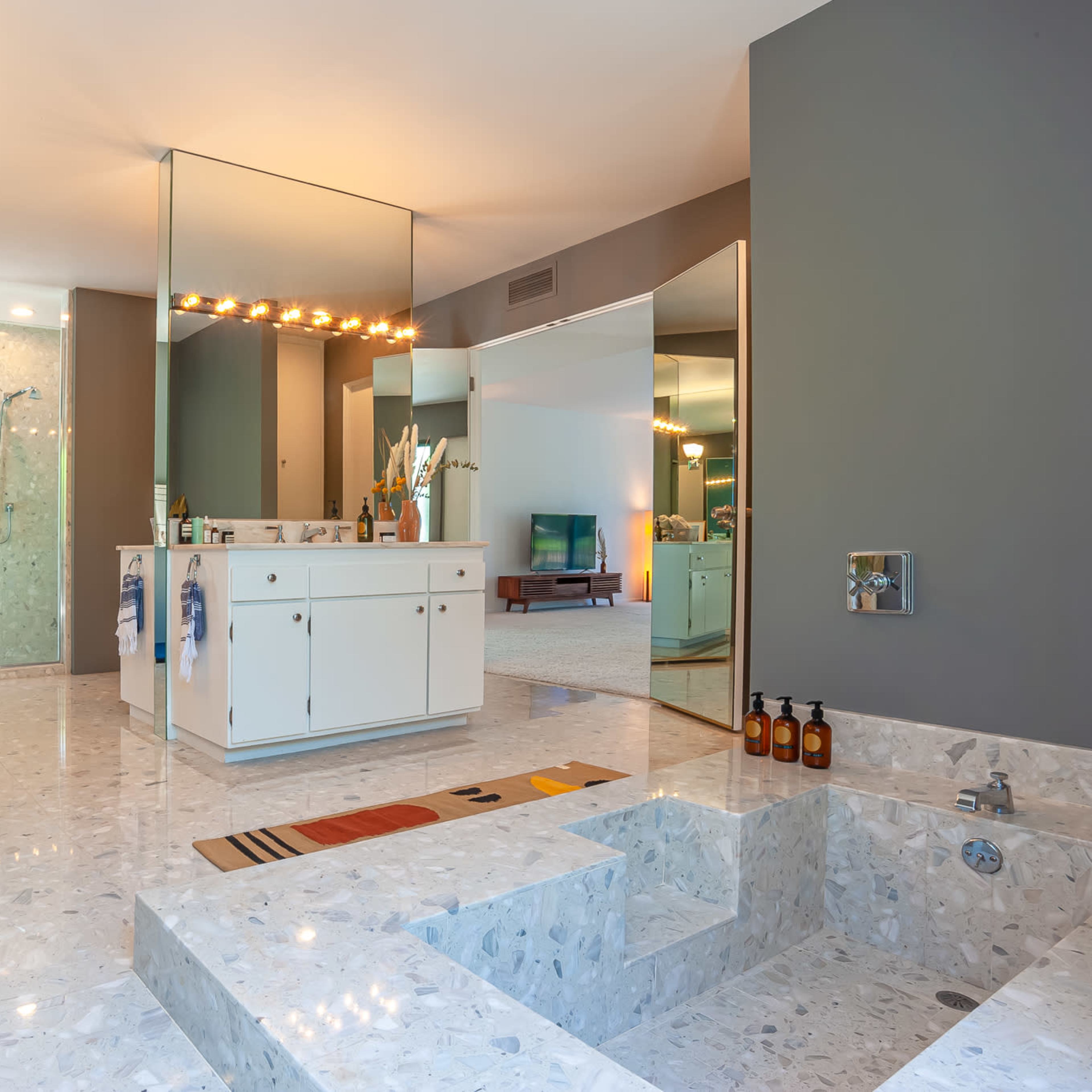 The bathroom features a spacious layout with a large mirror, double sink vanity, a walk-in shower, and a sunken tub surrounded by marble flooring.
