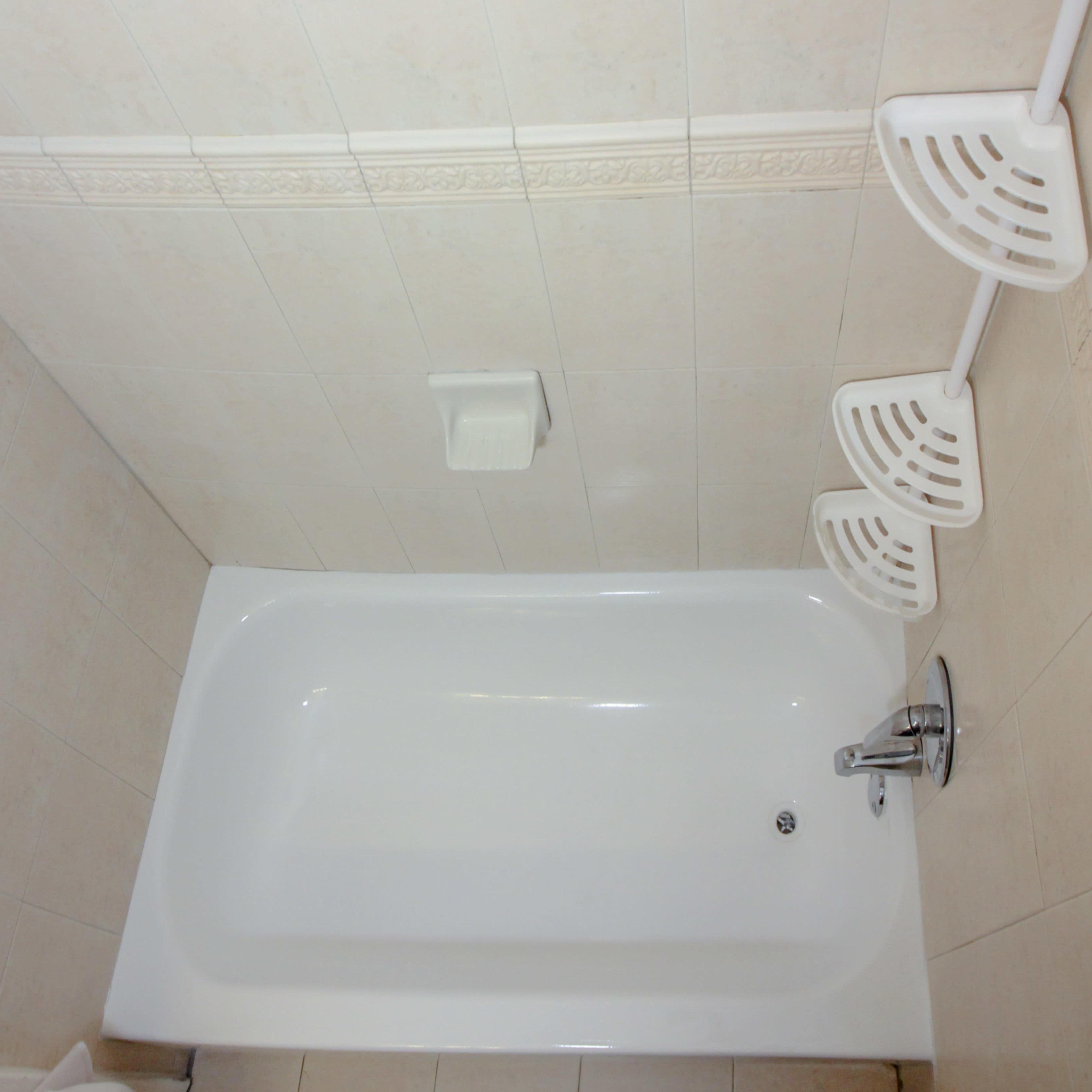 A clean, empty bathtub in a tiled bathroom with wall-mounted shelves.