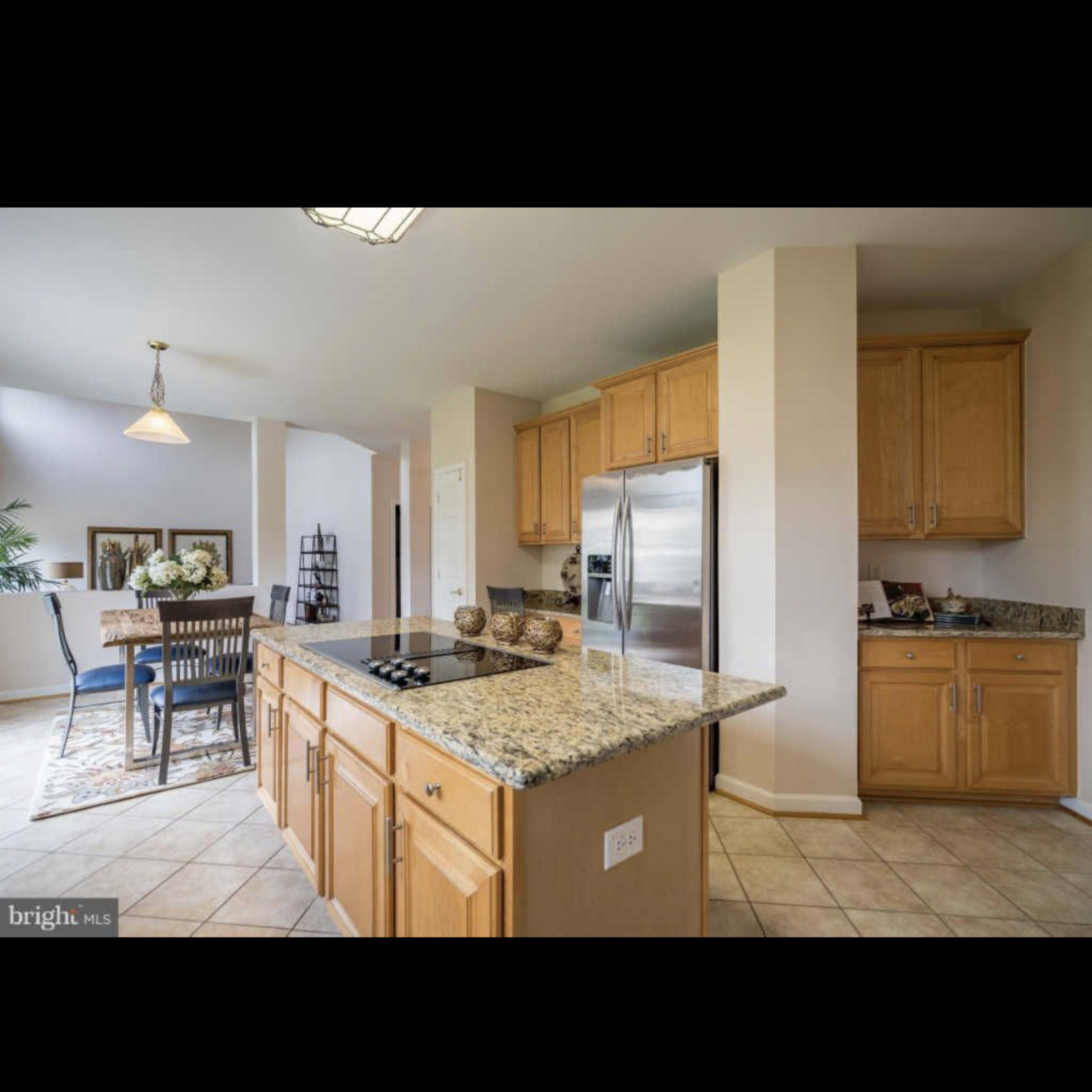 A modern kitchen features wooden cabinets, a granite countertop with a stove, and stainless steel appliances, adjacent to a dining area.