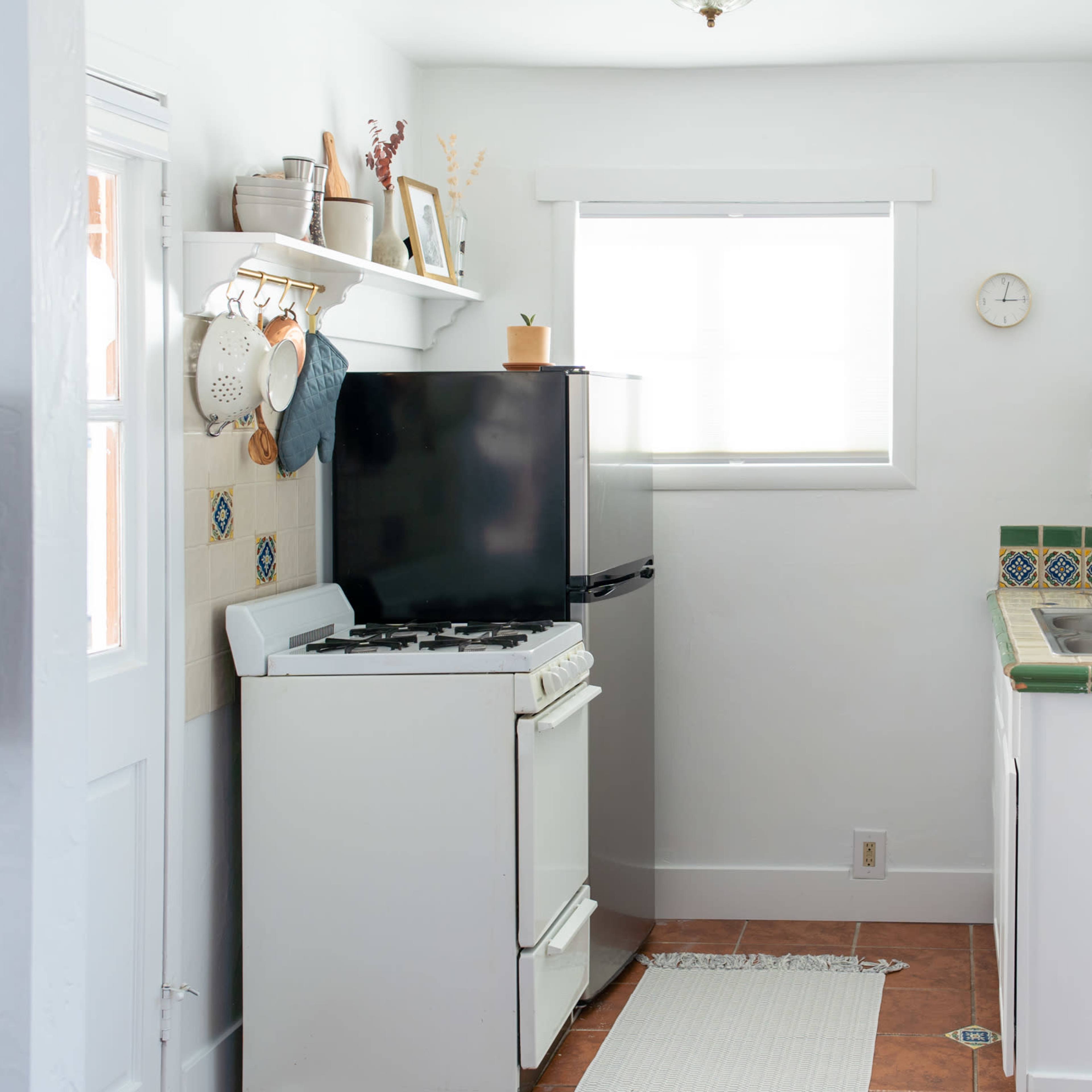 A compact kitchen featuring a black refrigerator, a white stove, a sink, and light-colored cabinetry against a tiled backsplash.