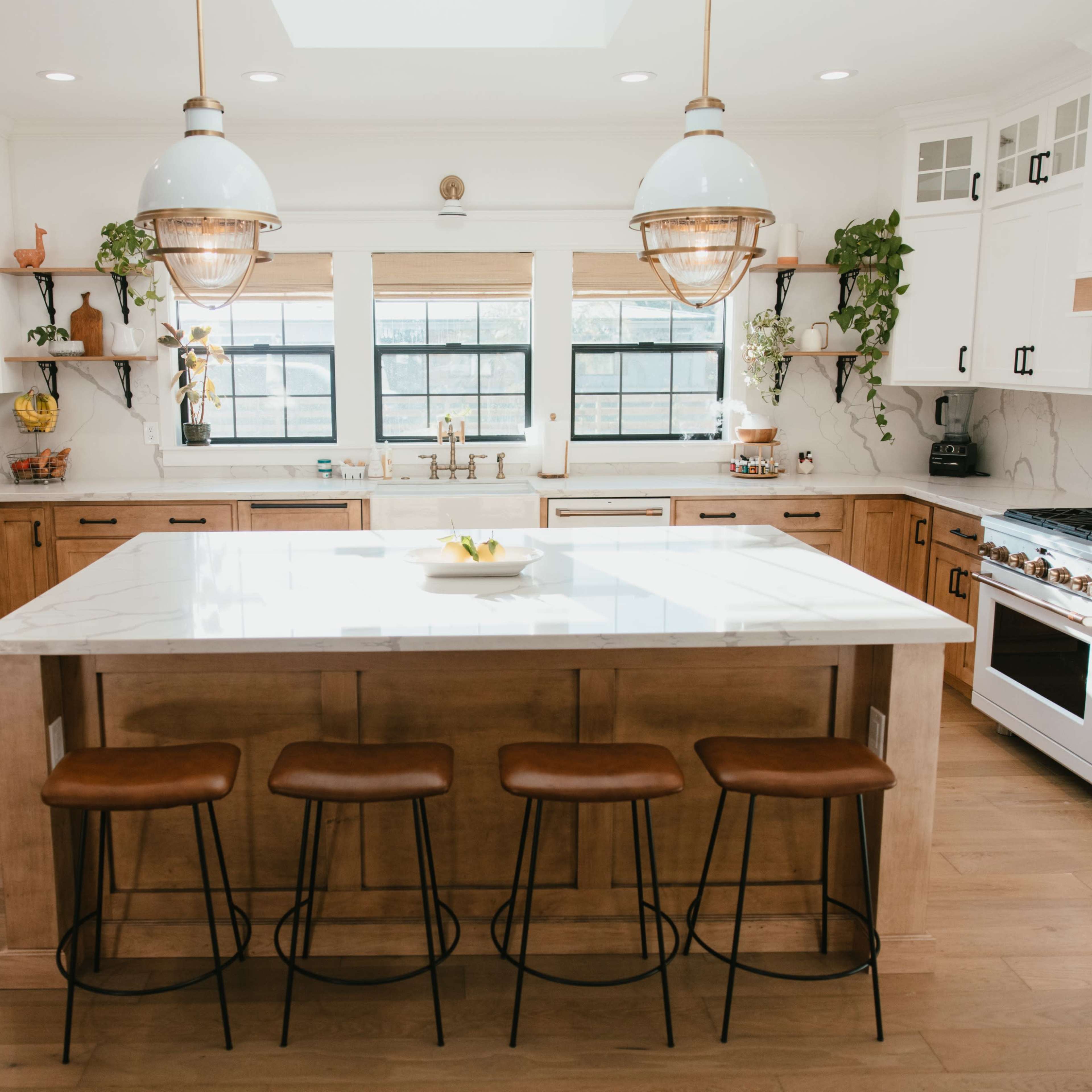 A modern kitchen features a large island with four stools, wooden cabinets, and pendant lighting above, creating a bright and functional space.