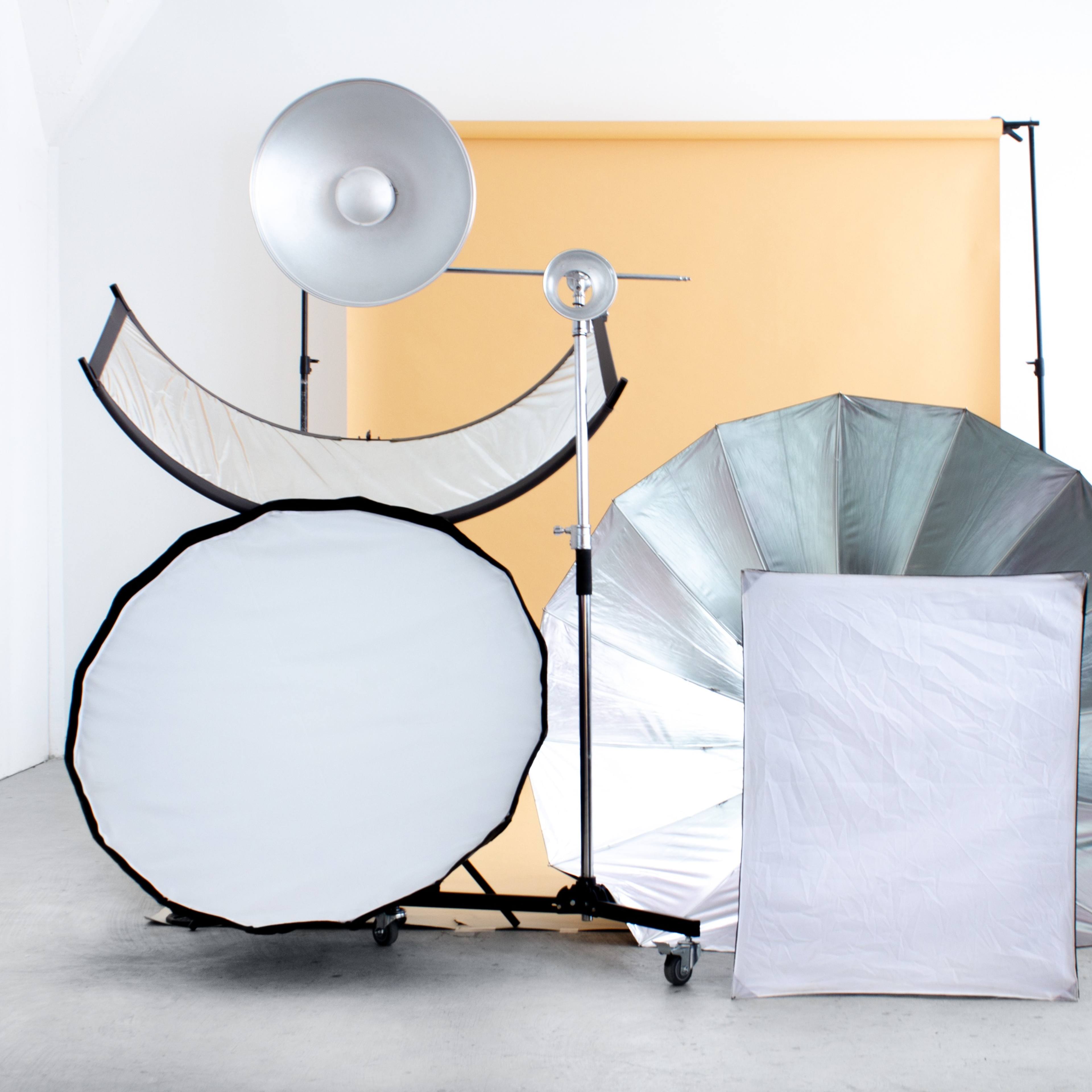 A photography setup with various light reflectors and diffusers arranged against a light orange backdrop in a spacious room.