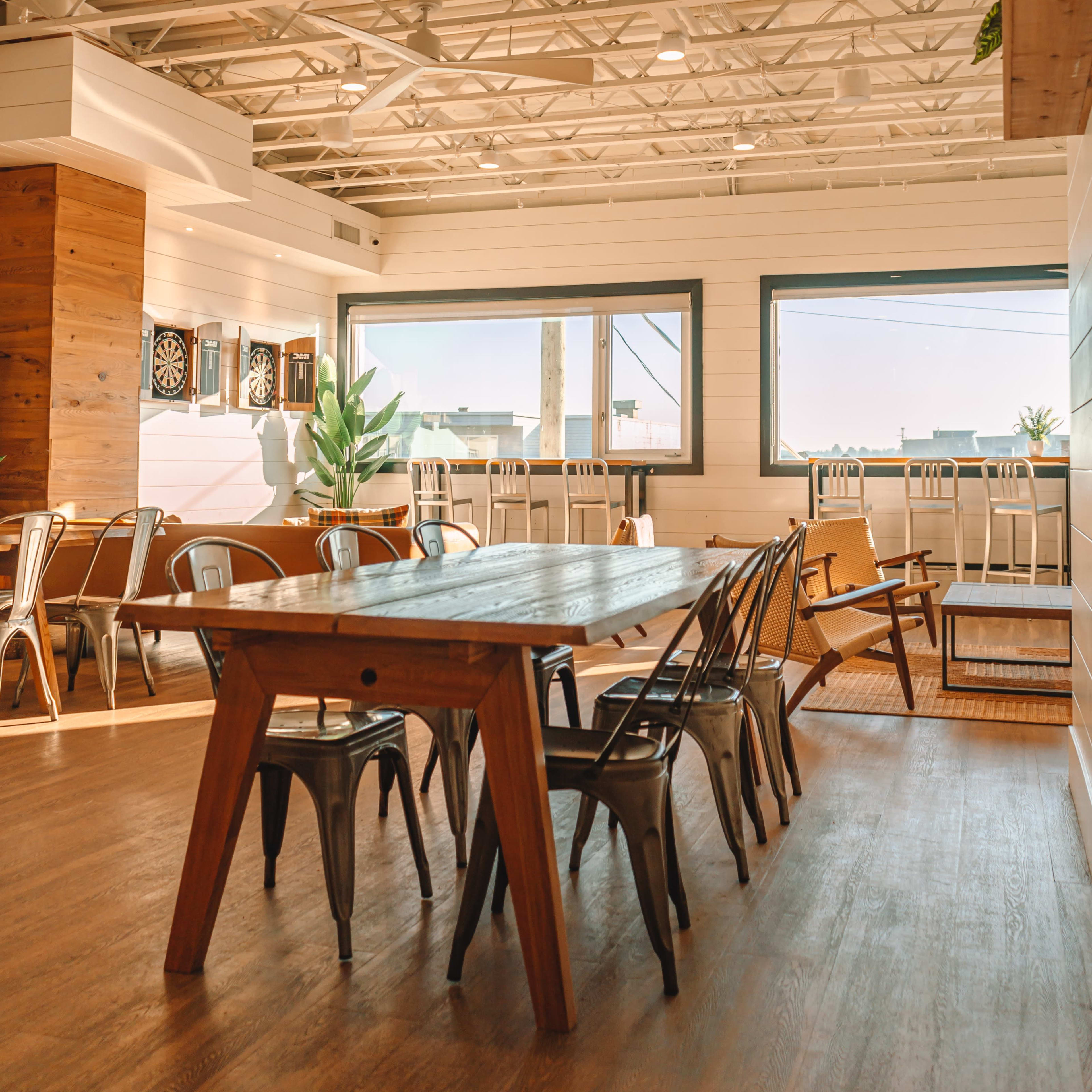 A spacious indoor dining area with wooden tables and metal chairs, large windows, and a bright, open layout.