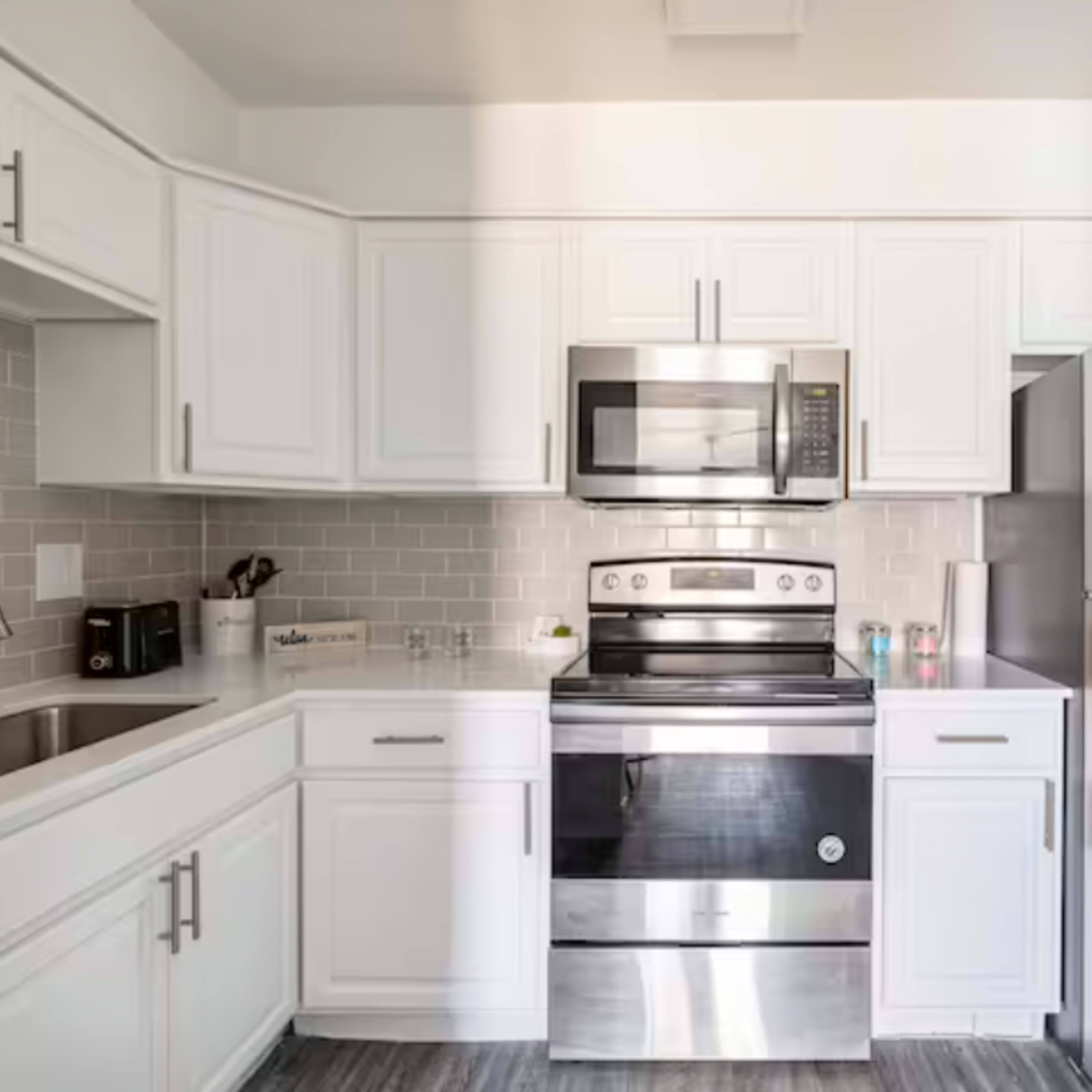 A modern kitchen with white cabinetry, stainless steel appliances, and a gray tiled backsplash.