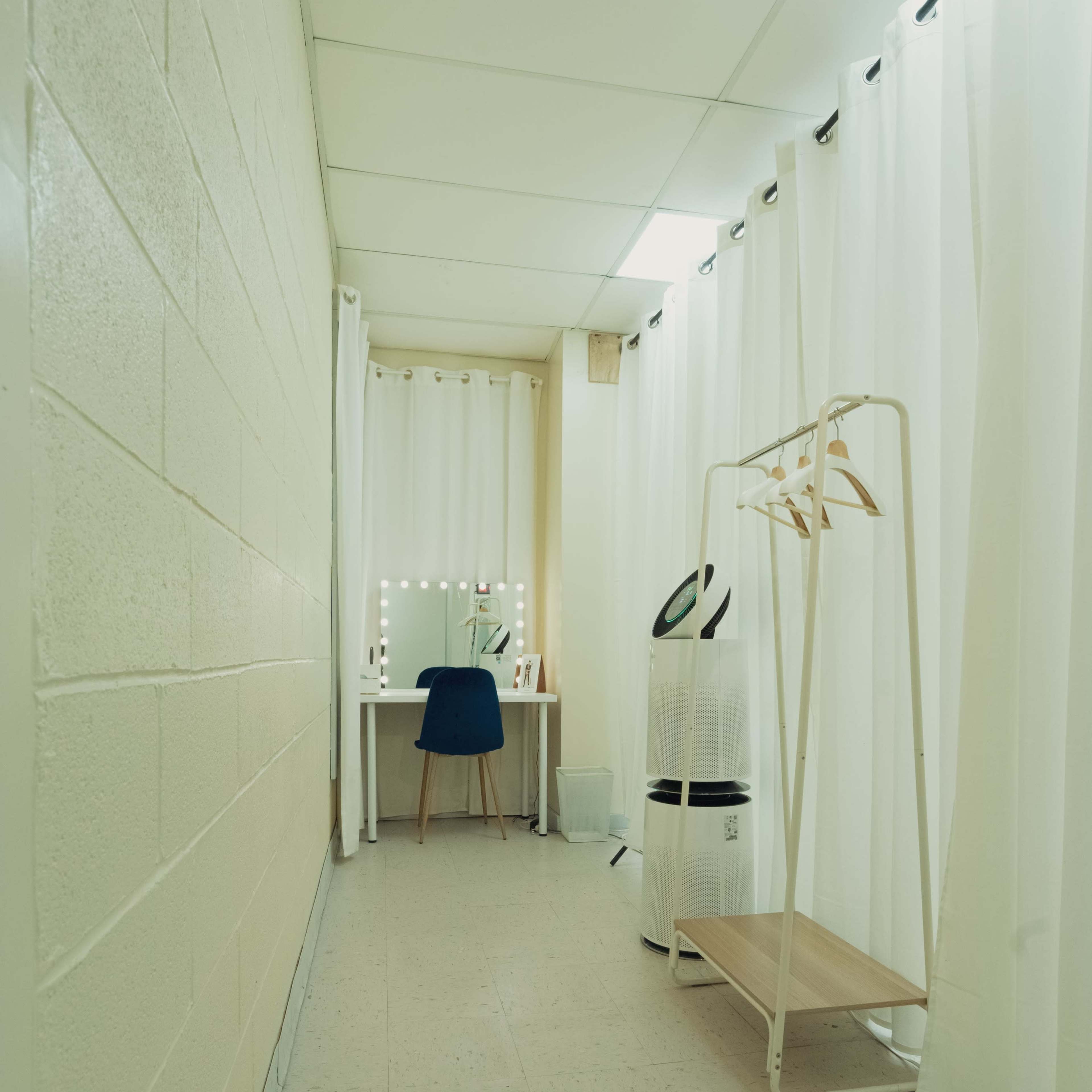 A narrow hallway with a dressing table, a chair, and a clothes rack behind curtains.