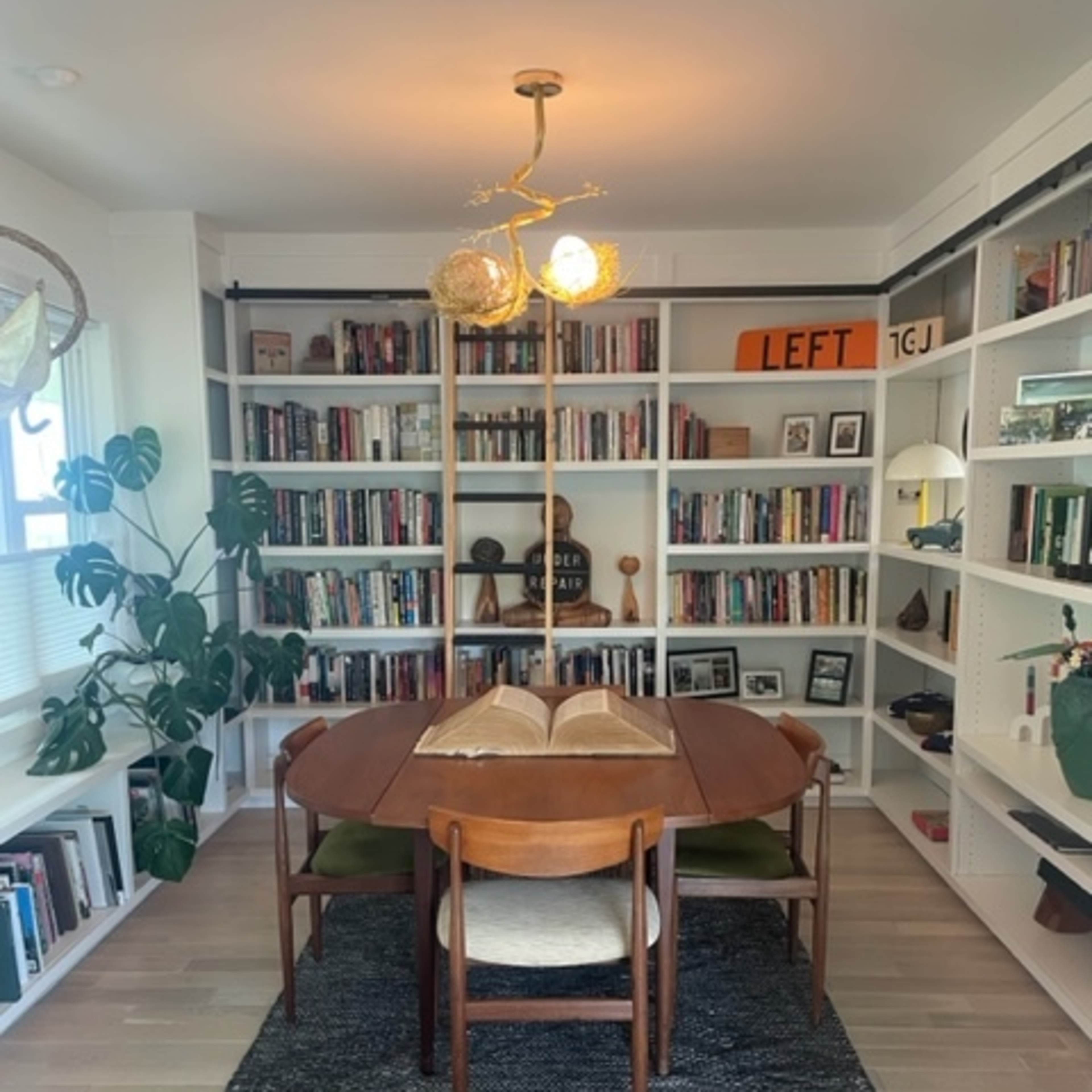 A dining table with wooden chairs is centered in a bright room surrounded by bookshelves filled with various books and decor items.