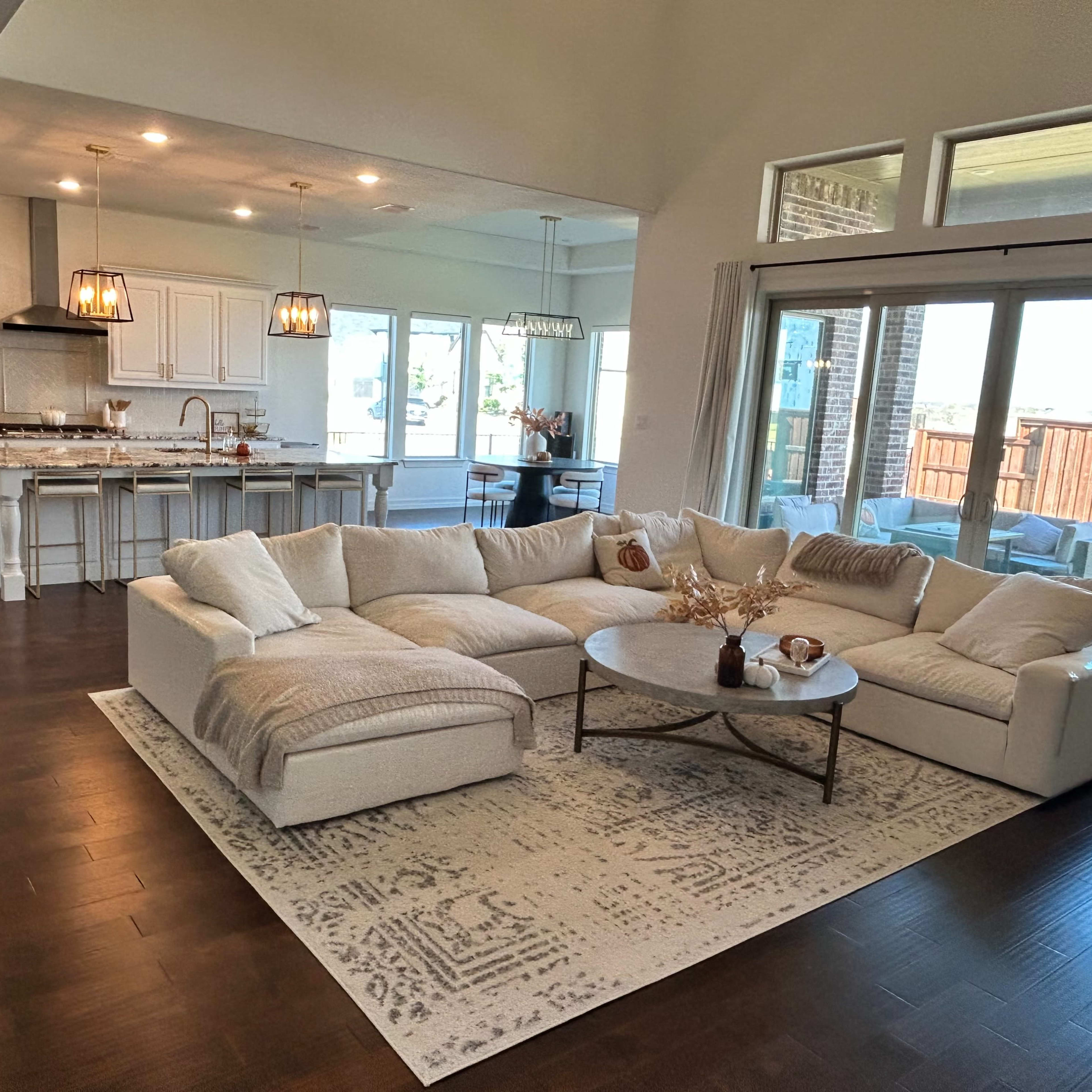 A spacious living room features a large sectional sofa, a central coffee table, and an open layout connecting to a modern kitchen.