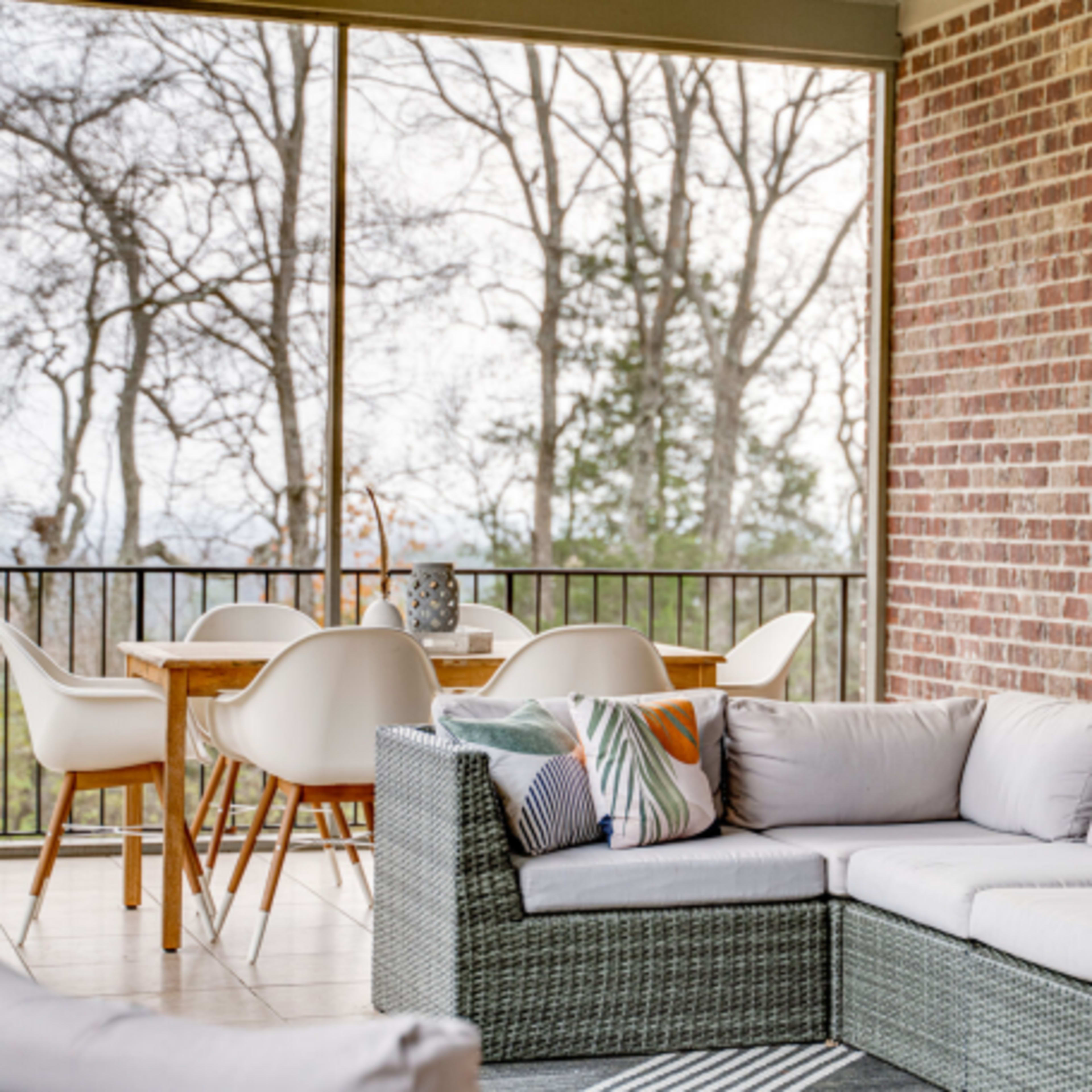 A covered patio with a sectional sofa and a dining table surrounded by chairs, set against a backdrop of bare trees.