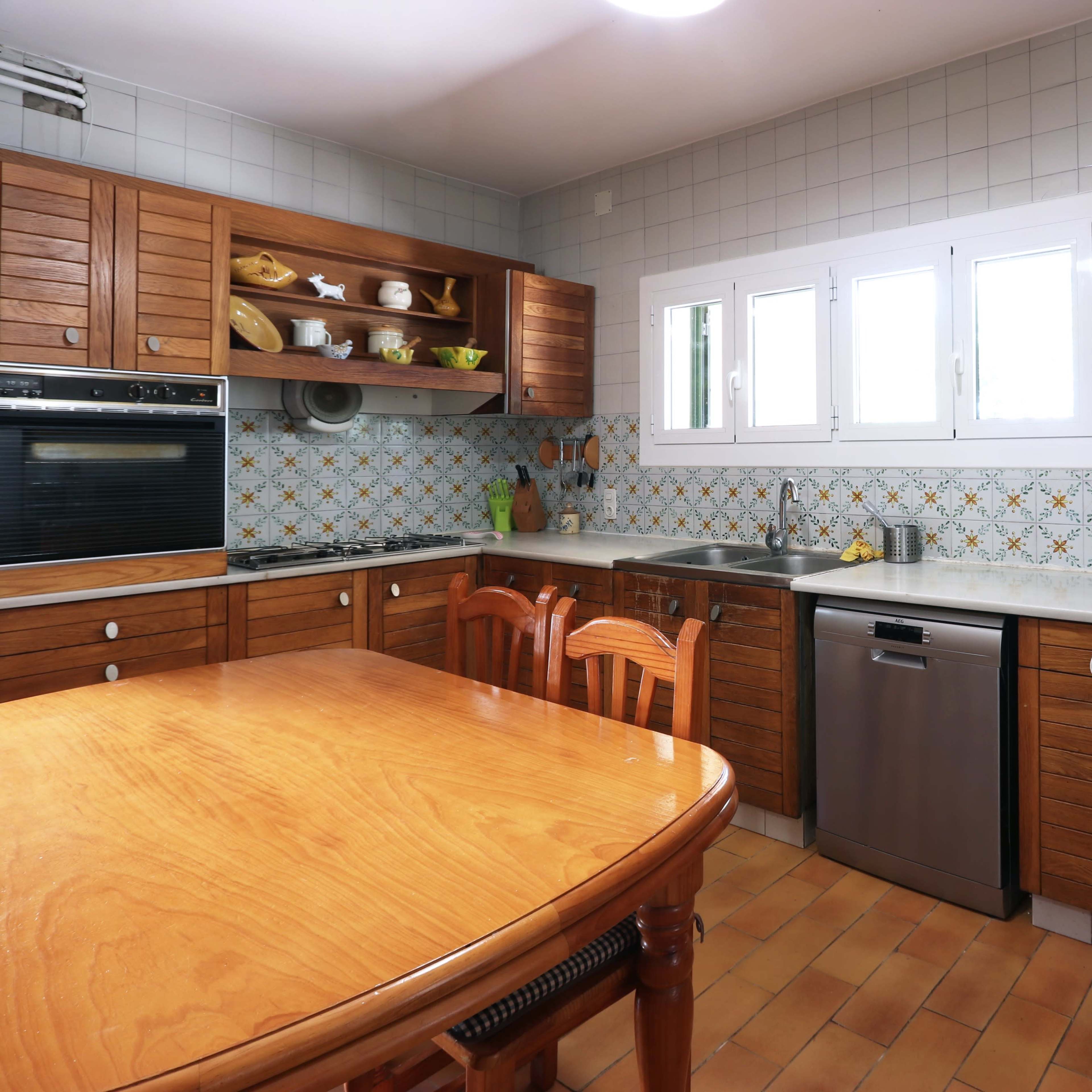 The kitchen features wooden cabinets, a marble countertop, and a dining table surrounded by four chairs, with decorative tiles on the walls.
