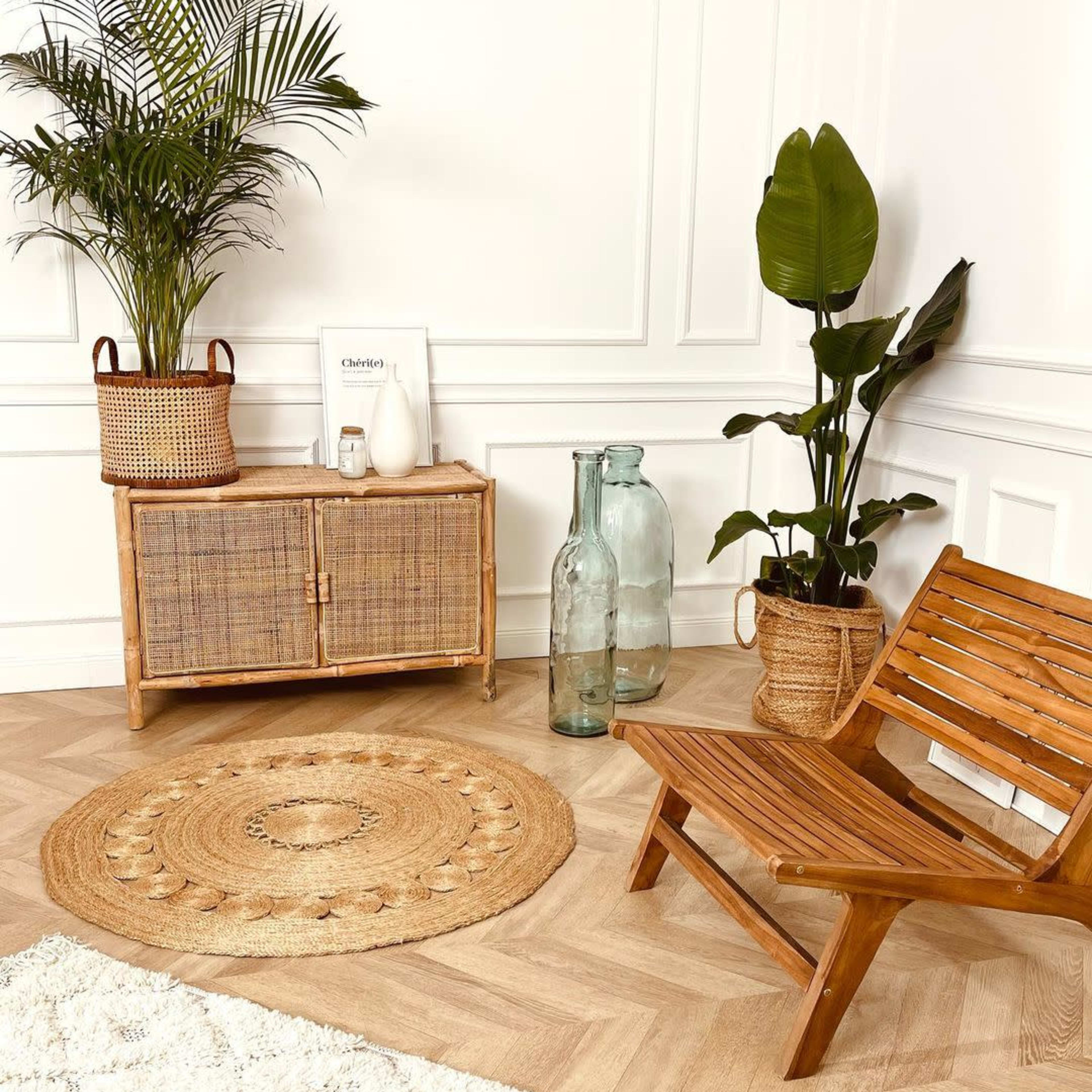 A cozy corner featuring a wooden chair, a rattan cabinet, potted plants, and decorative bottles on a patterned rug.