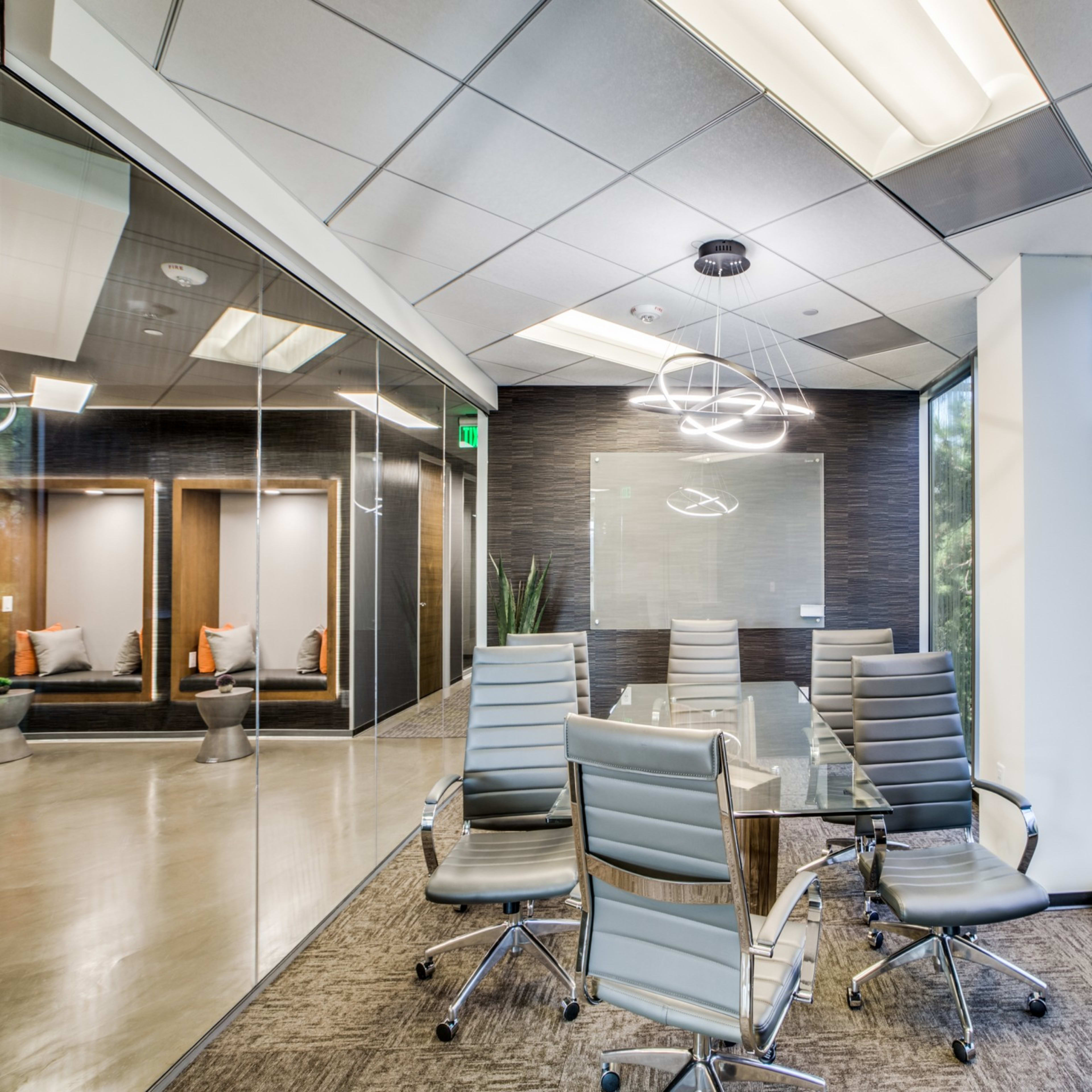 A modern conference room features a glass table surrounded by ergonomic chairs, with large windows providing a view of the outdoors.