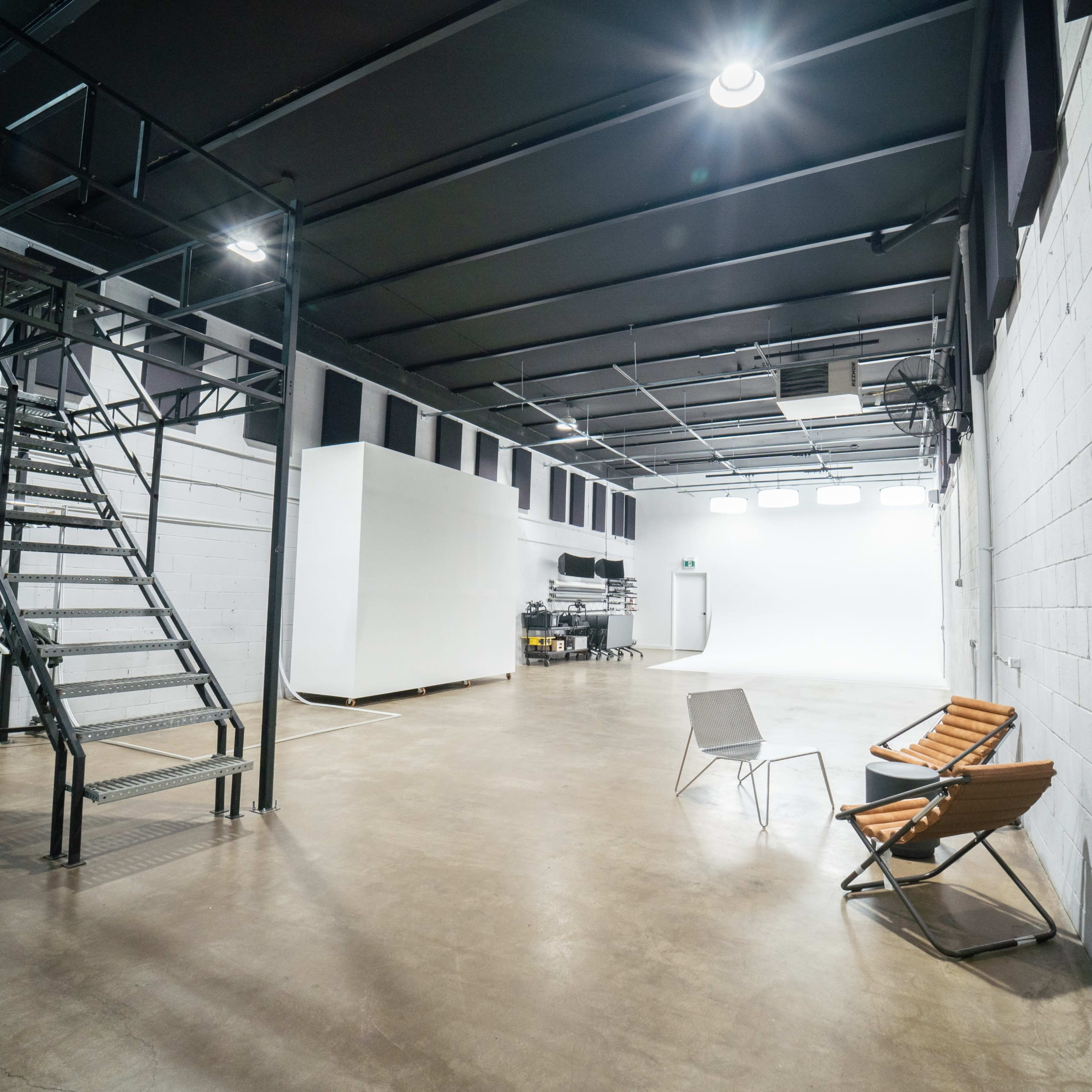 A spacious, industrial-style room with concrete walls, a staircase, and two folding chairs.