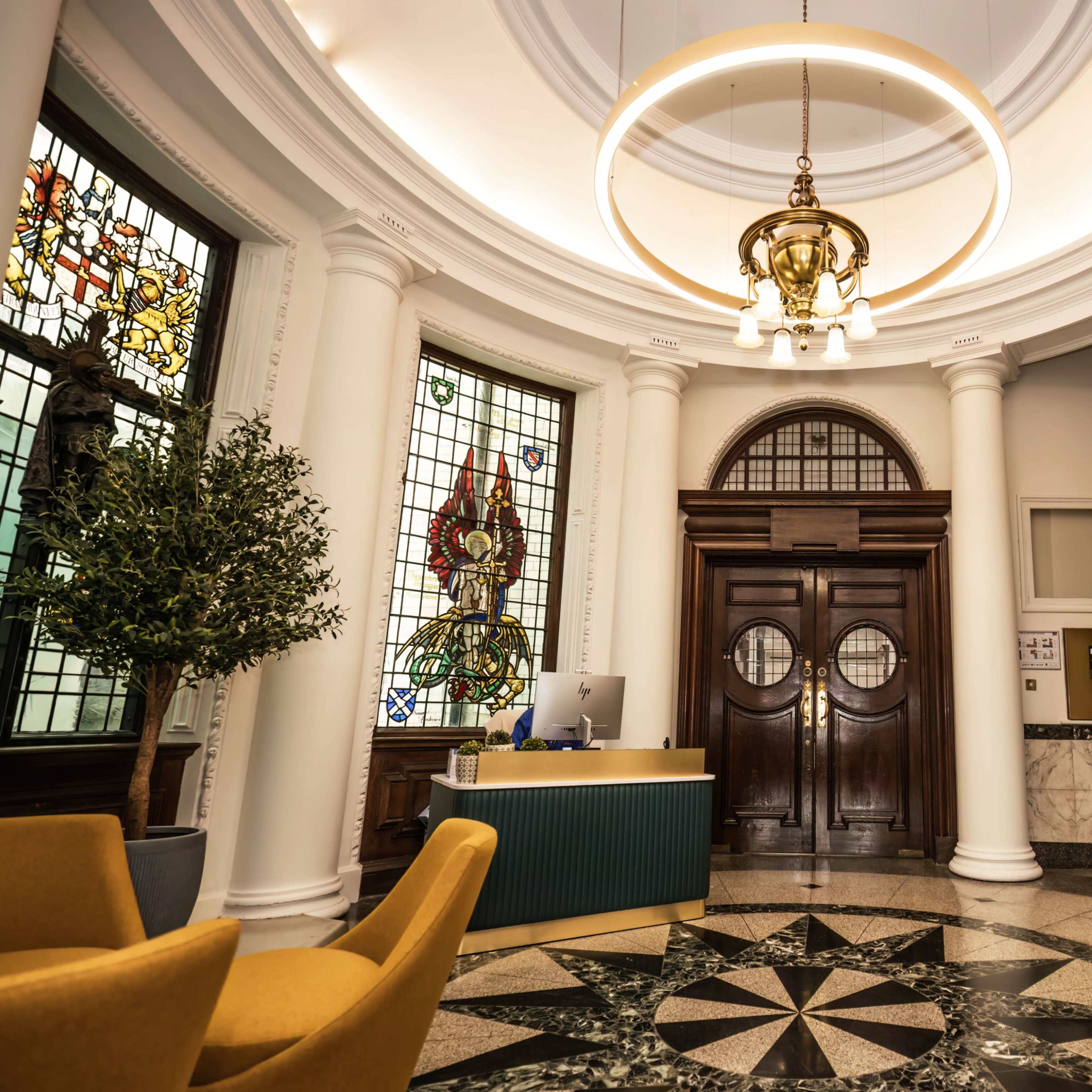 A lobby with ornate columns, a circular chandelier, stained glass windows, and a reception desk.