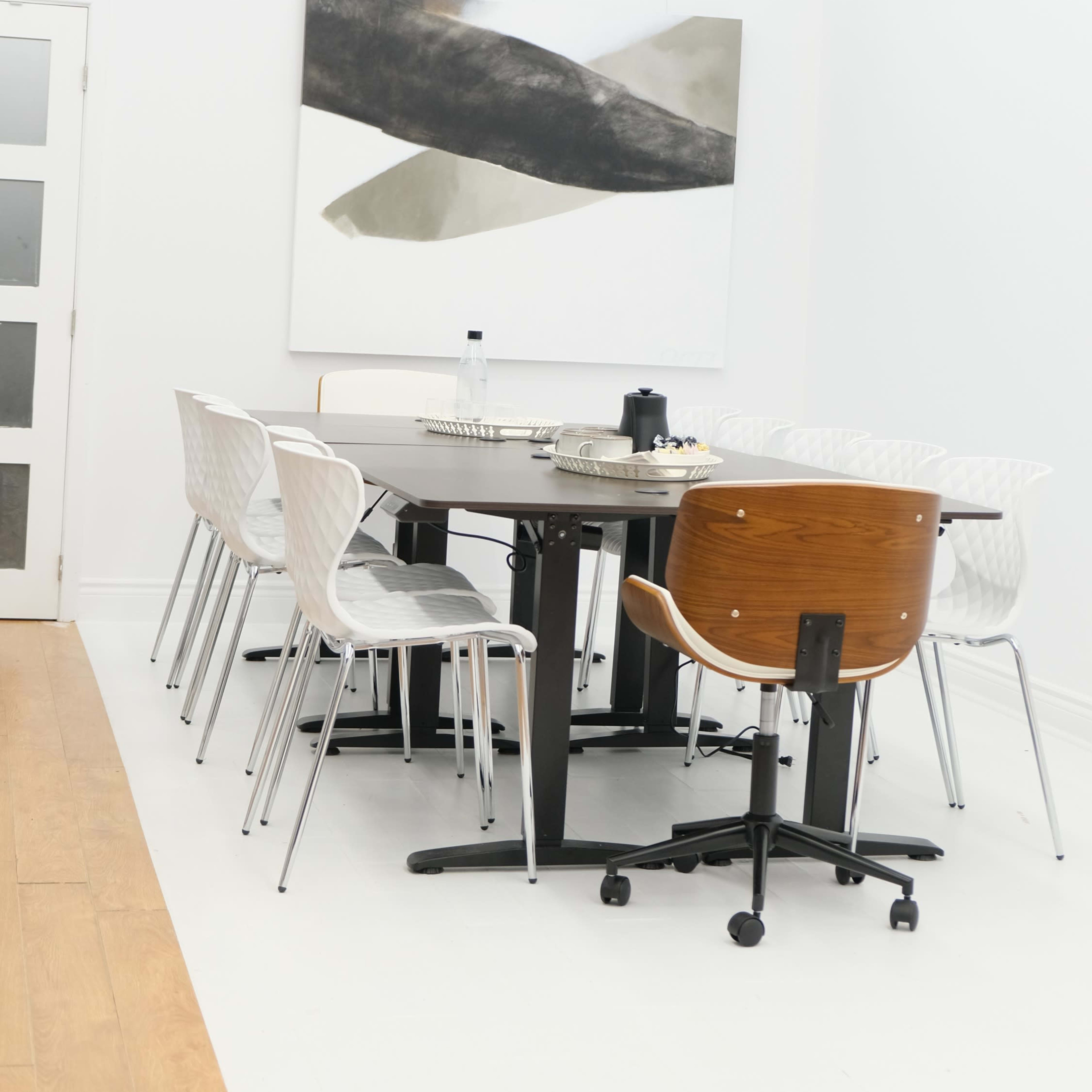 A modern dining area features a round black table surrounded by white and wooden chairs, with a large abstract painting on the wall.