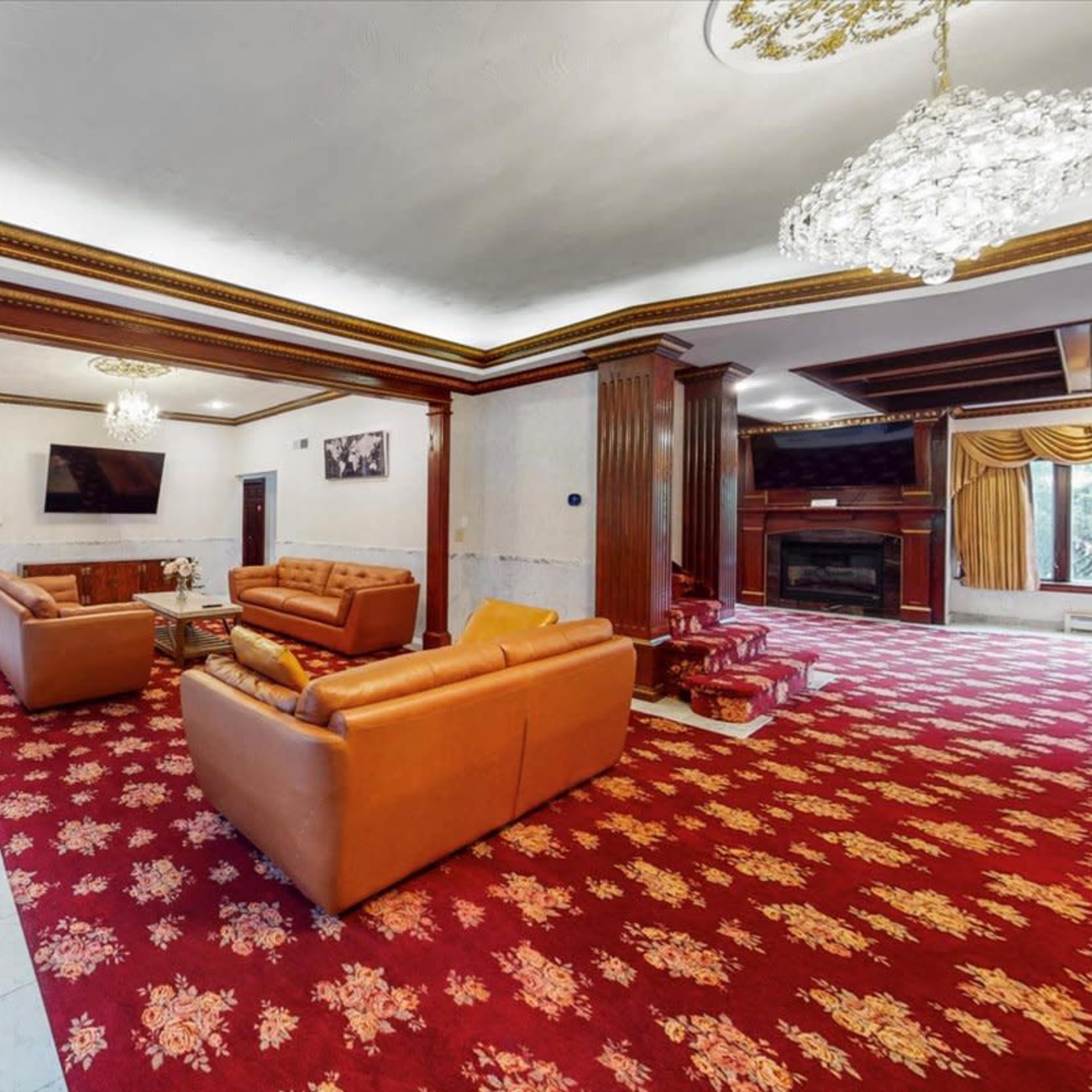 A spacious living room with leather sofas, a patterned carpet, and a fireplace, accented by decorative chandeliers and wooden paneling.