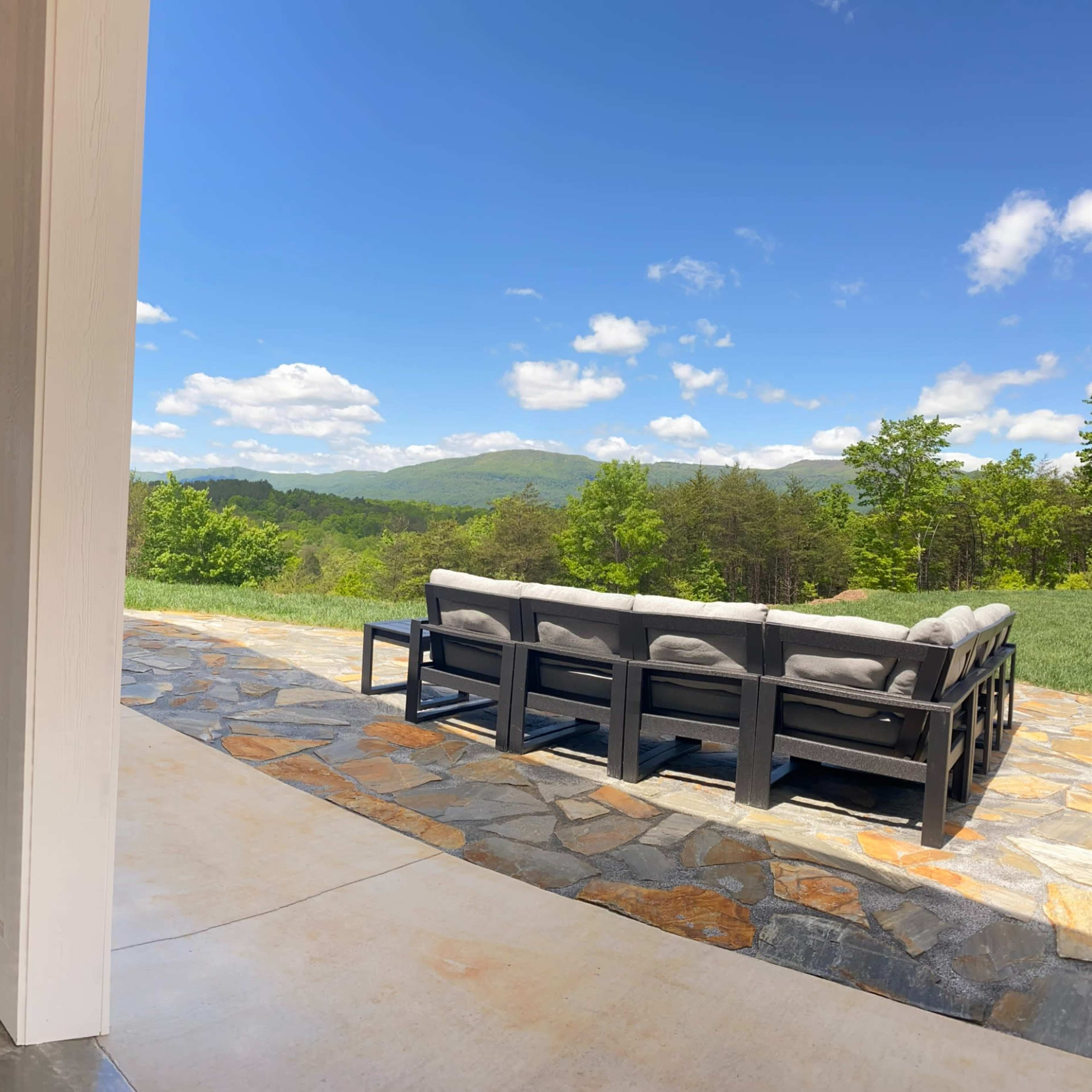 A spacious interior with polished concrete floors and a large window that opens to a view of mountains and a patio area with outdoor seating.