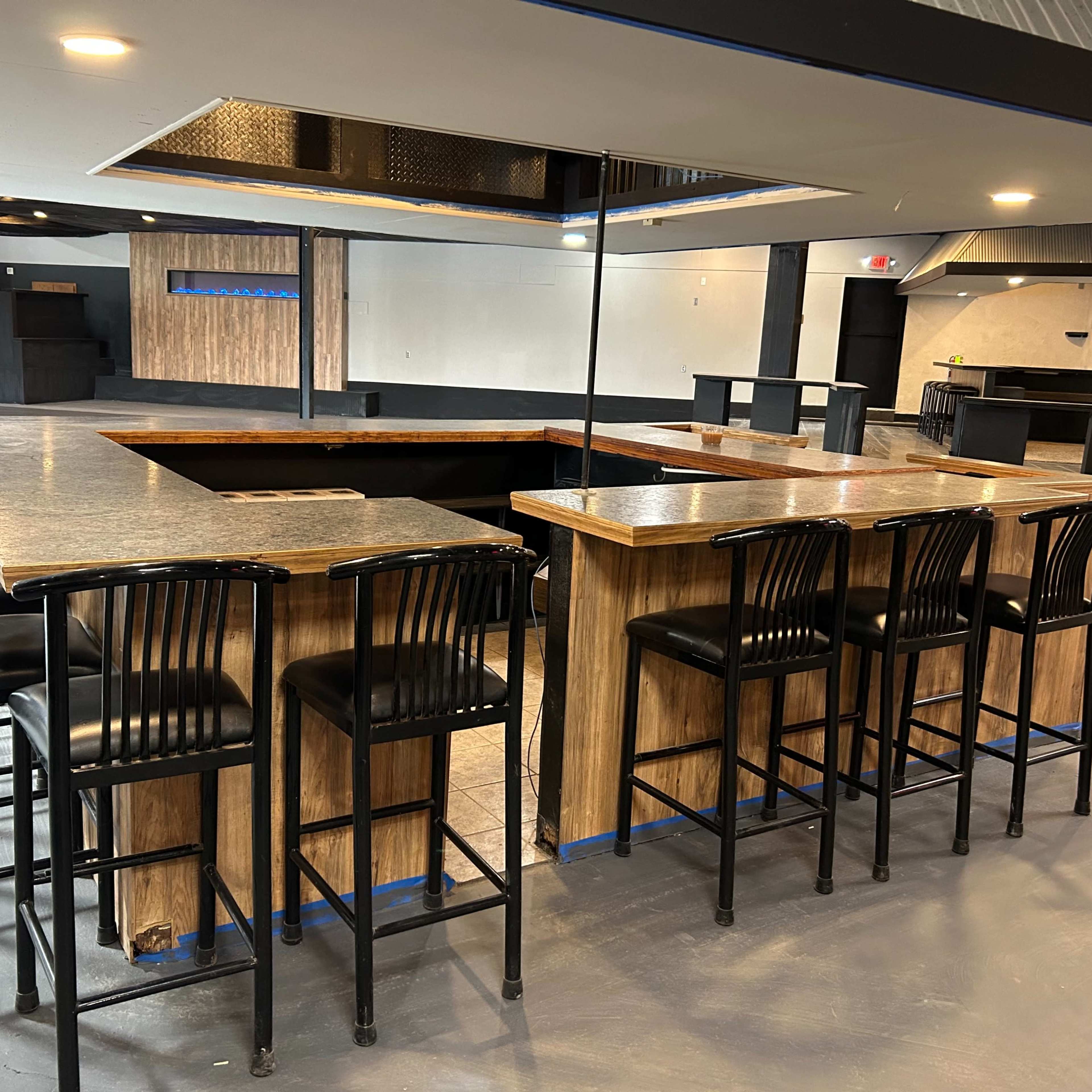 A modern, empty bar area with a wooden counter and black bar stools arranged around it.