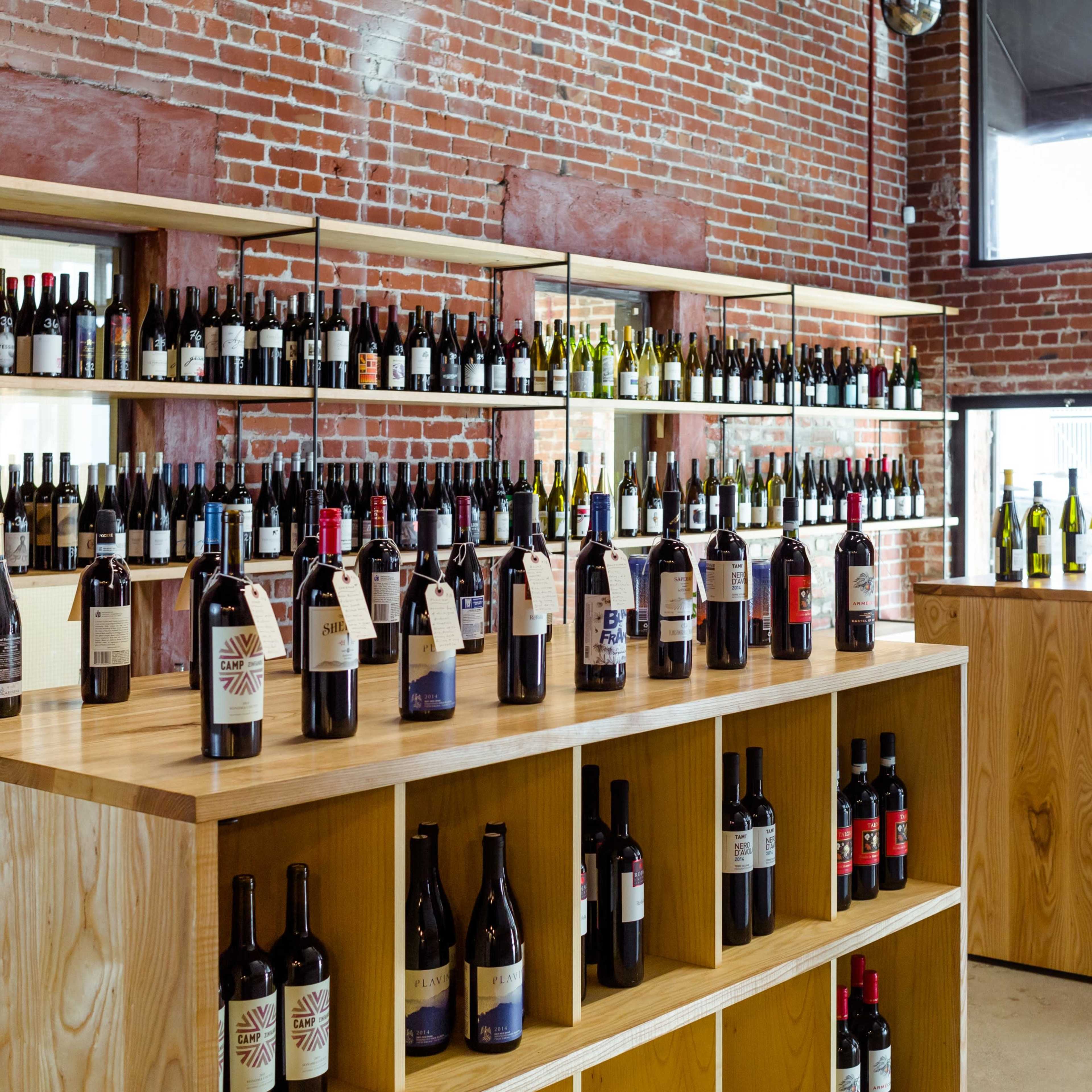 A modern wine shop with wooden shelving displaying a wide variety of wine bottles against a backdrop of exposed brick walls.