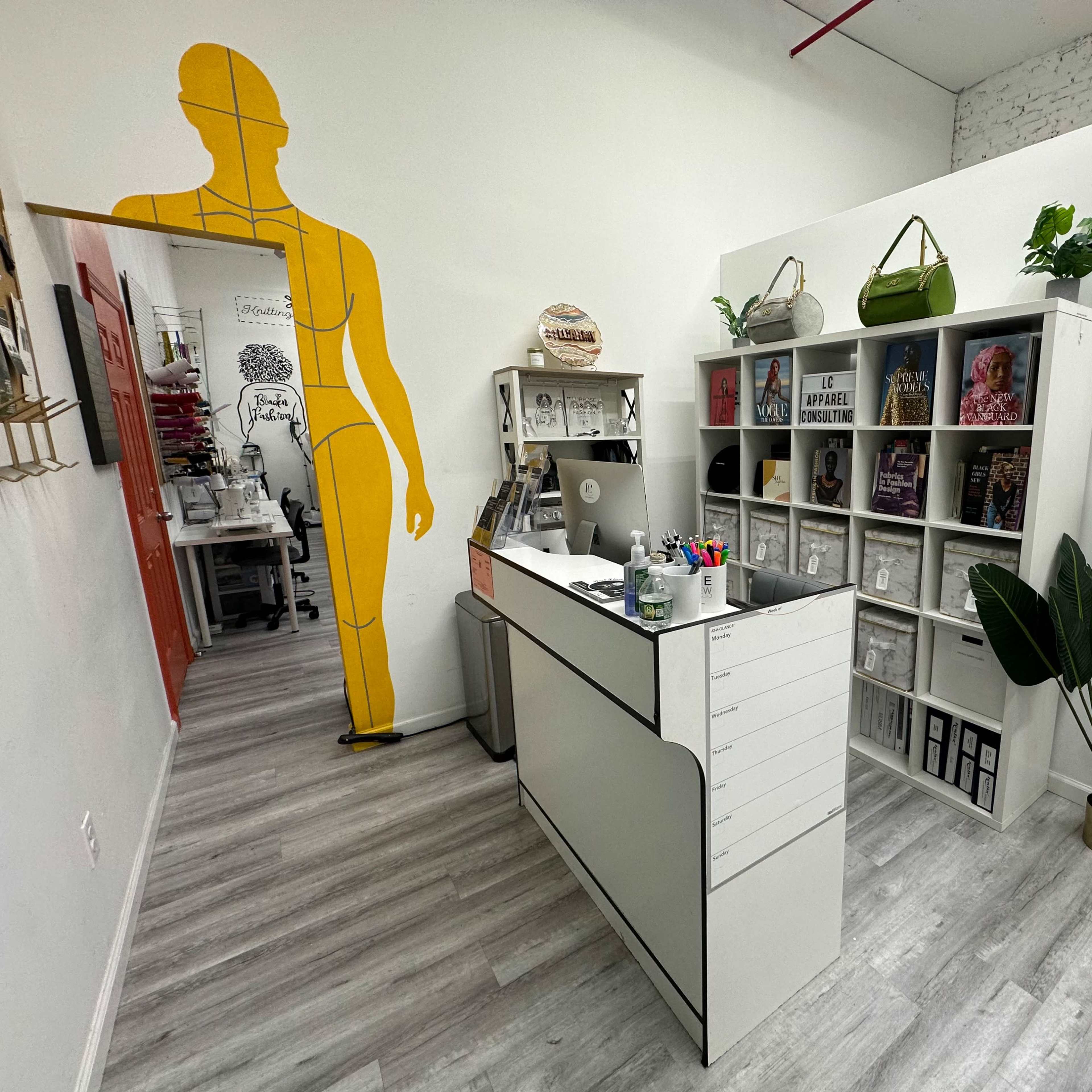 A modern interior workspace featuring a reception desk, shelving with books and decor, and a large wall graphic of a human figure.