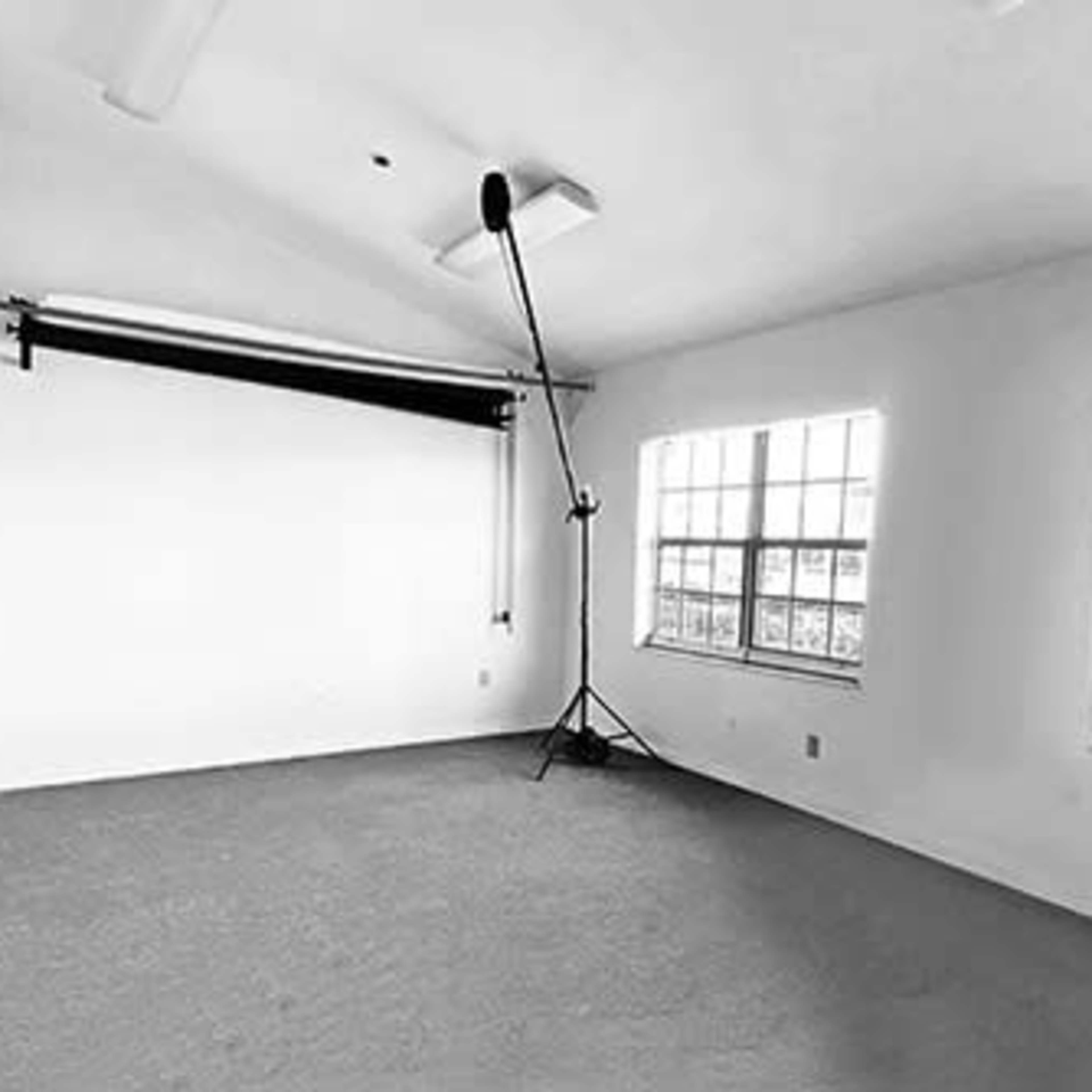 A sparsely furnished room with two large windows and a backdrop support stand in the corner.