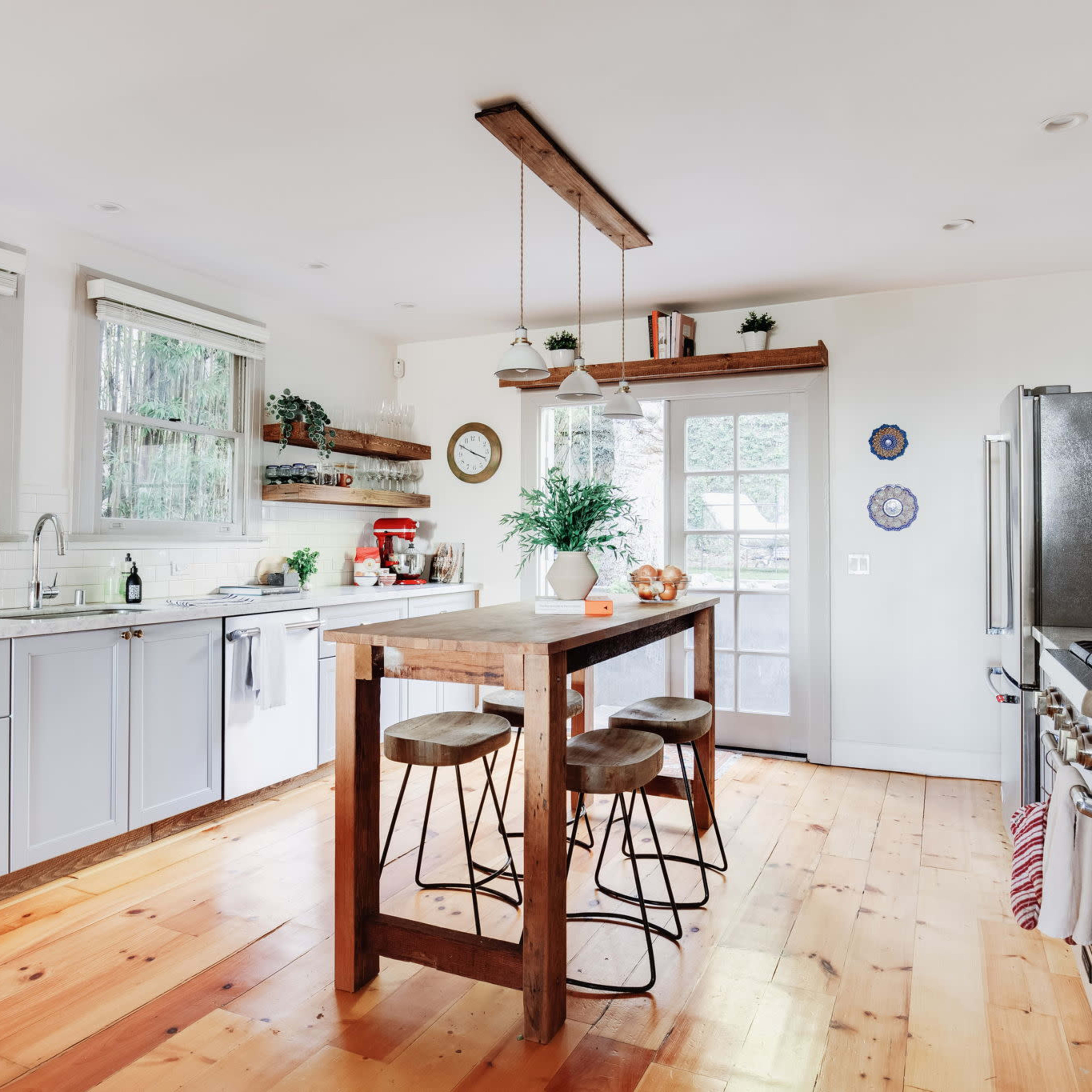 A modern kitchen features light cabinetry, a wooden island with stools, and large windows that allow natural light to illuminate the space.