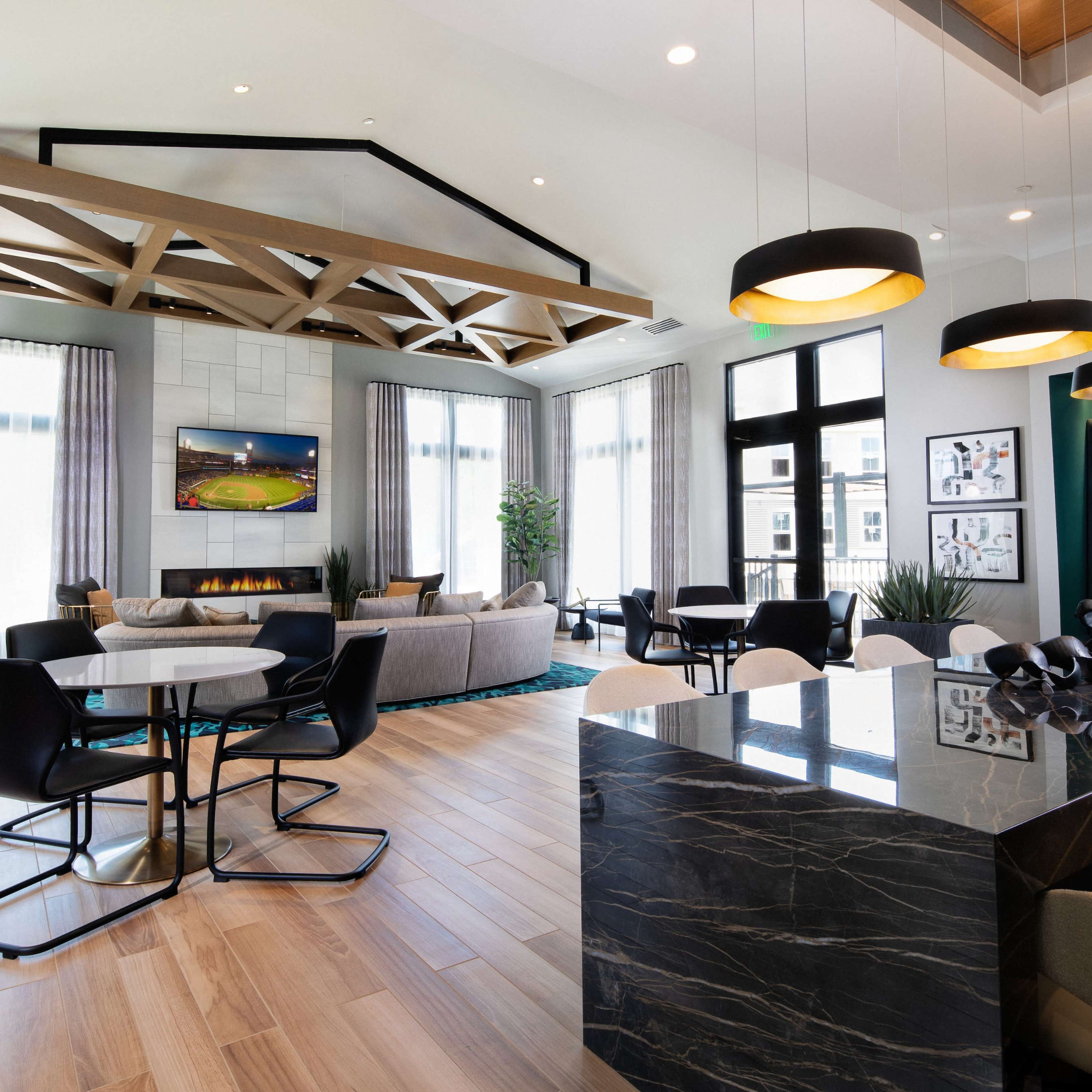 A modern lounge area with large windows, wooden ceiling beams, a television, and various seating arrangements.