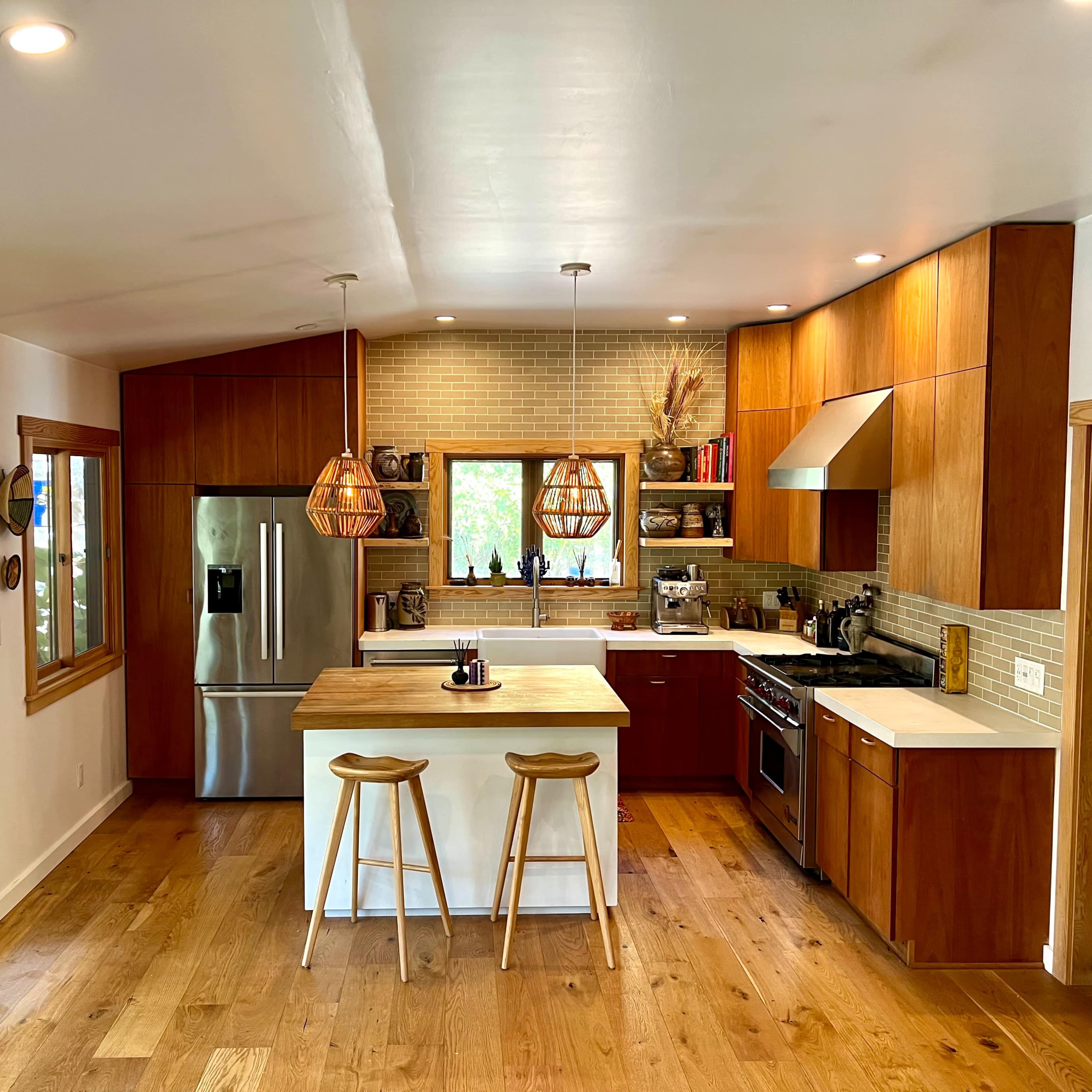 A modern kitchen features wooden cabinetry, a large island with two stools, and pendant lighting above a spacious countertop.