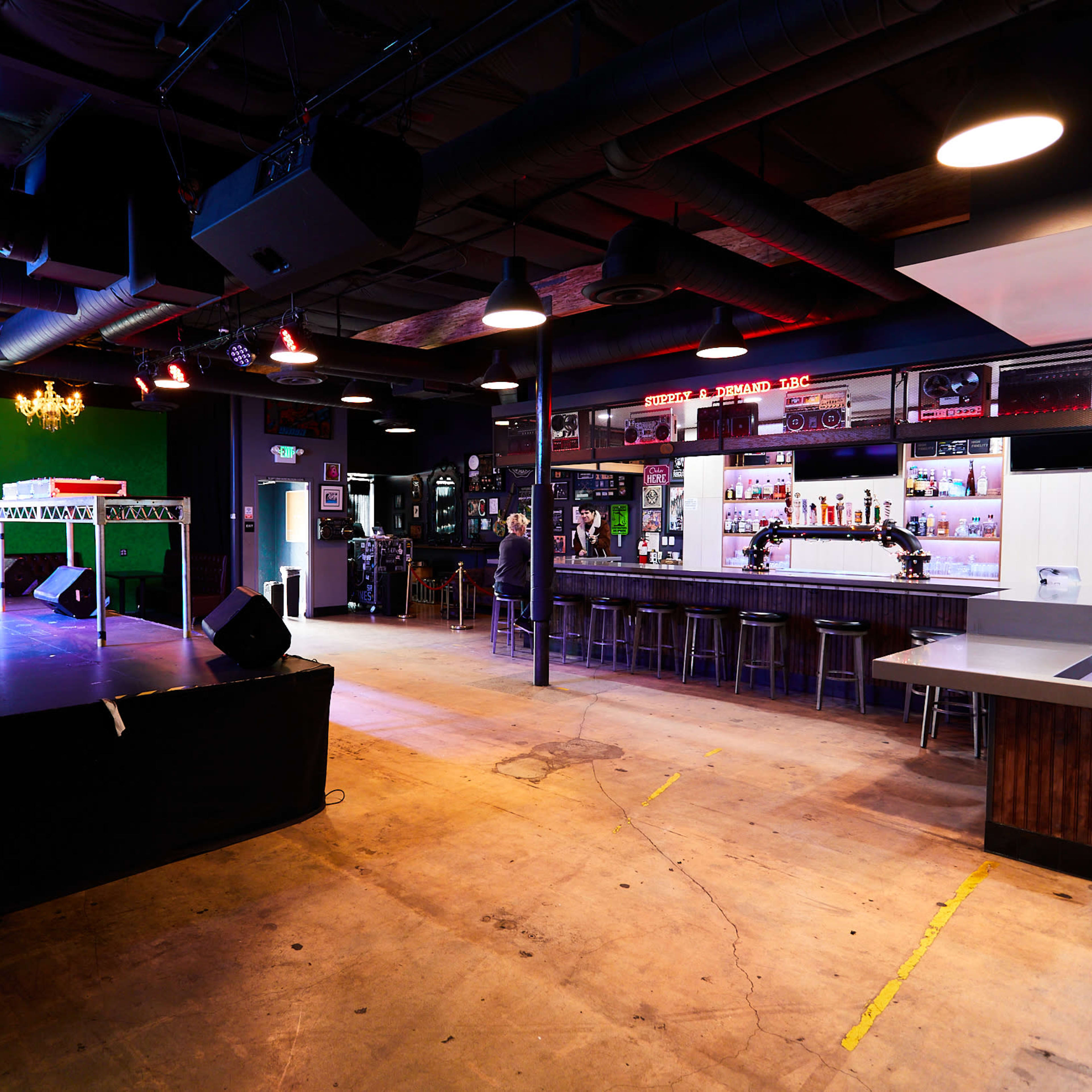 An empty stage area with musical equipment and a bar in a dimly lit performance venue.