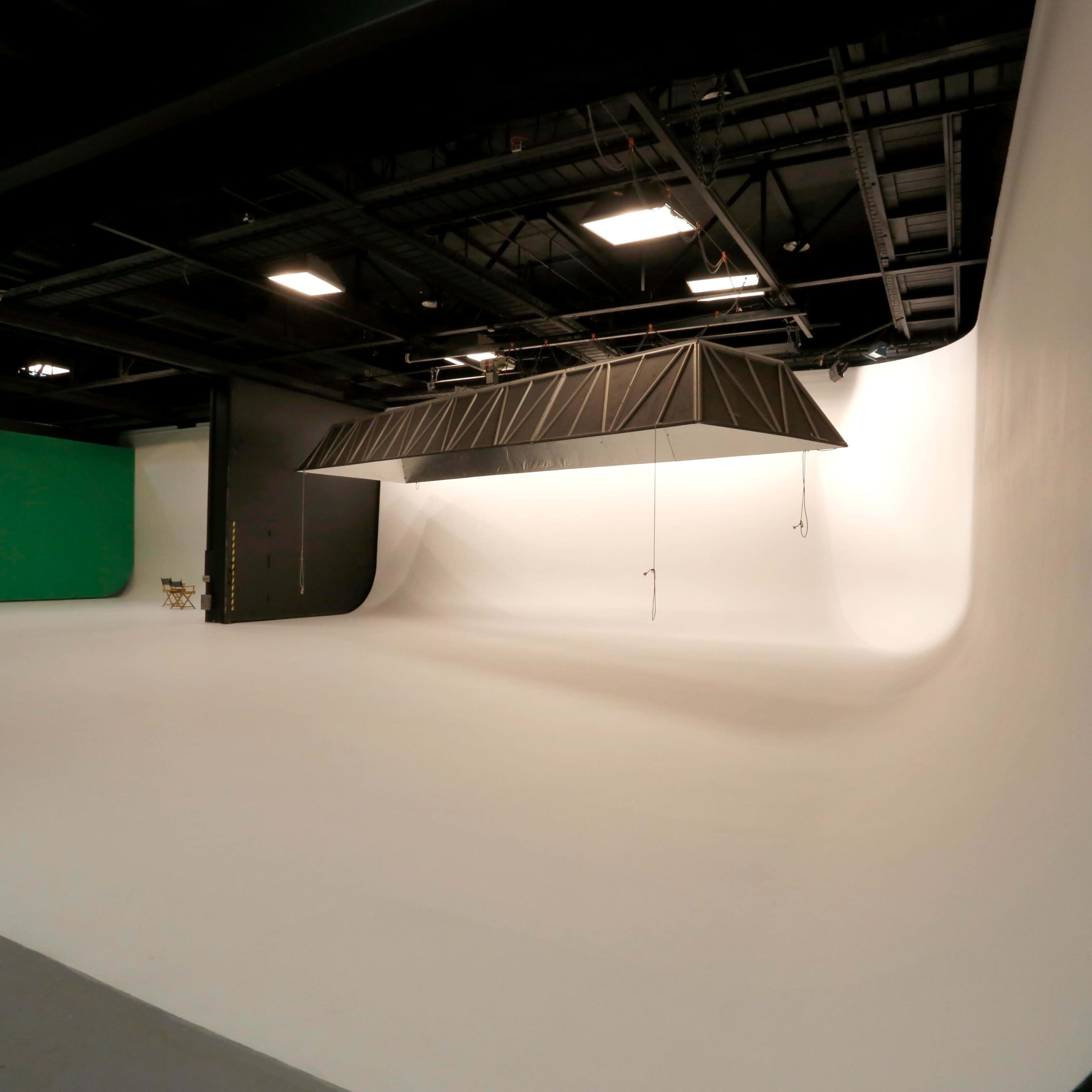 A spacious photography studio with a seamless white backdrop and a green screen on one side.