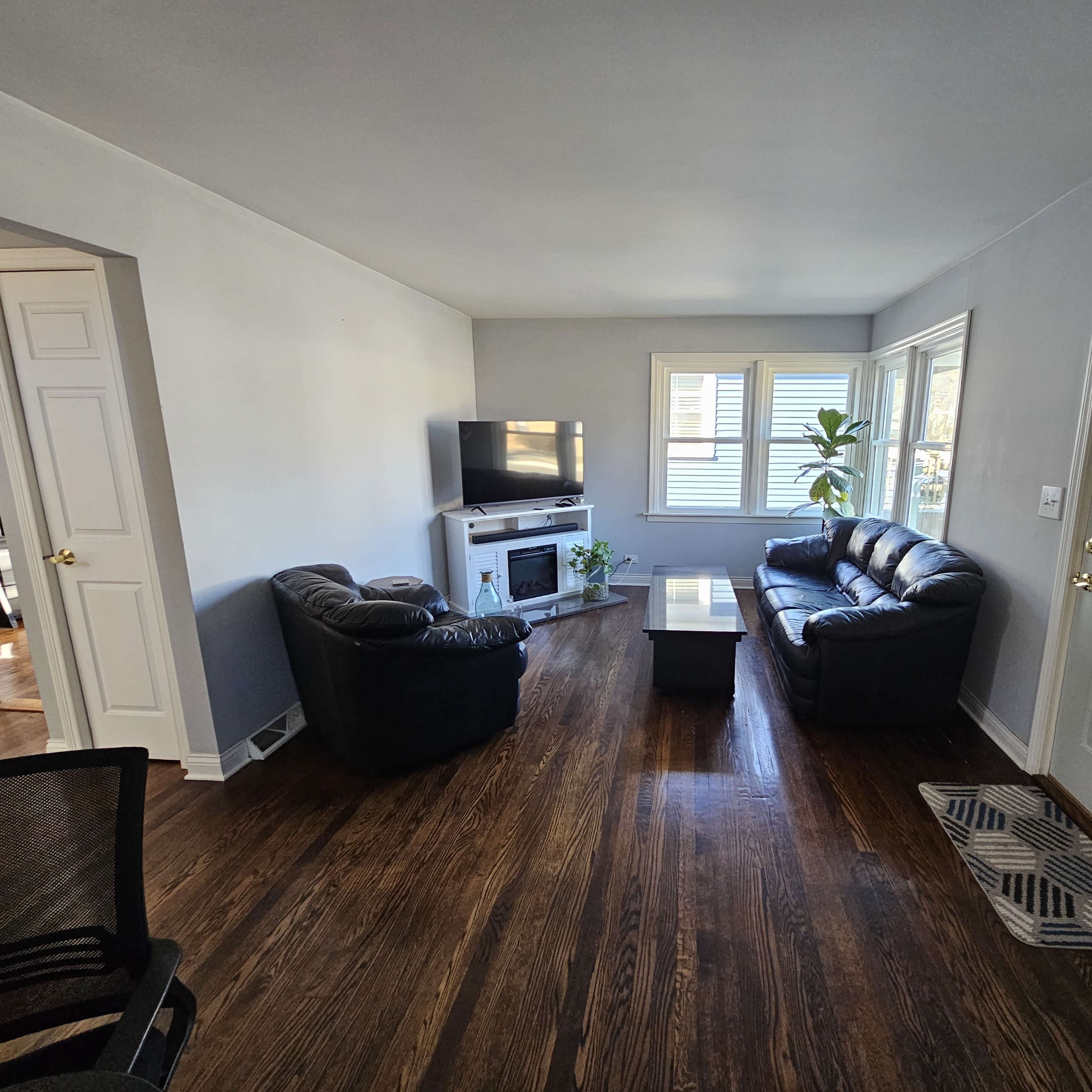 The living room features two black leather couches facing each other, a coffee table in the center, and a television mounted on the wall beside a window.