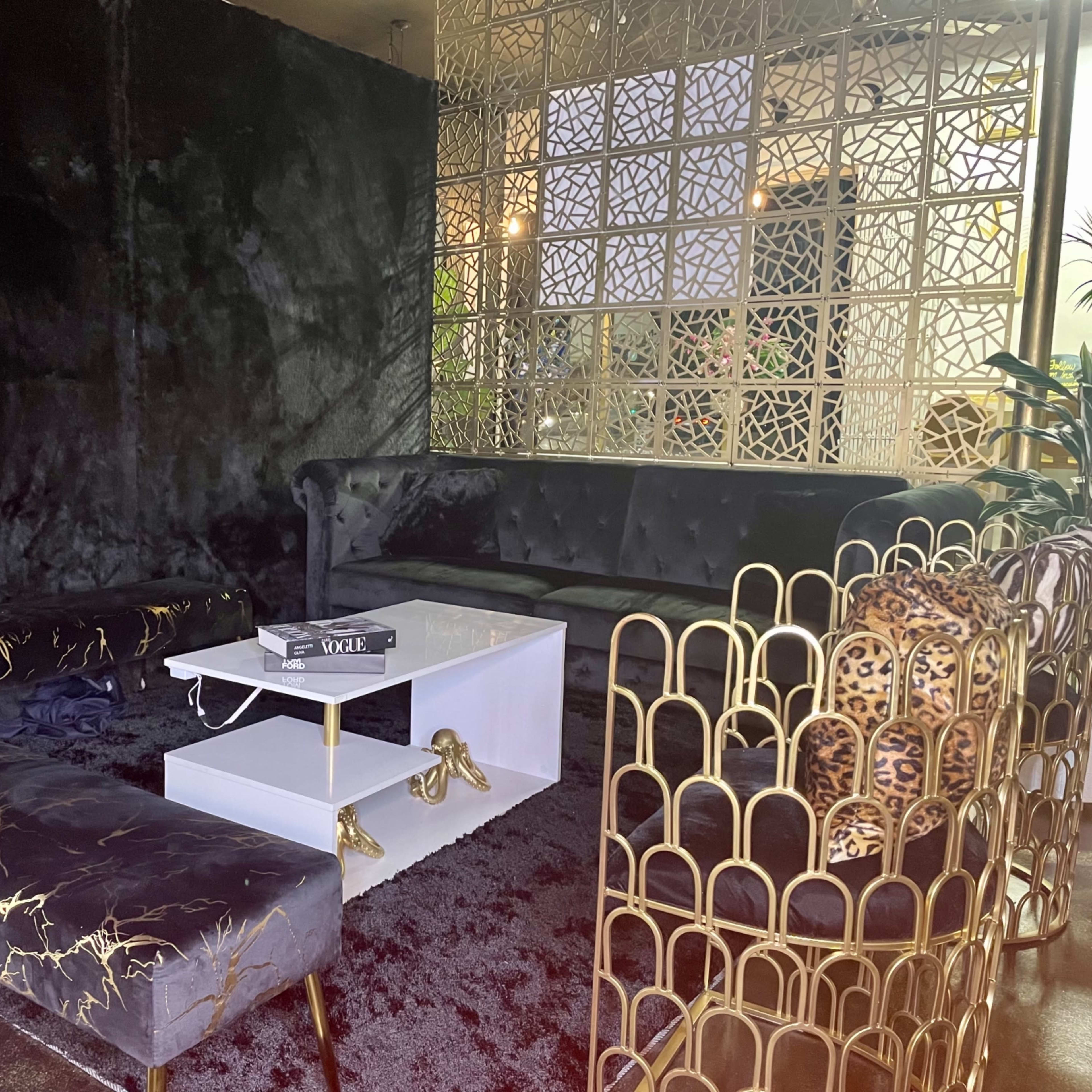 A modern lounge area with black velvet furniture, a glass coffee table, and a decorative golden screen reflecting light.