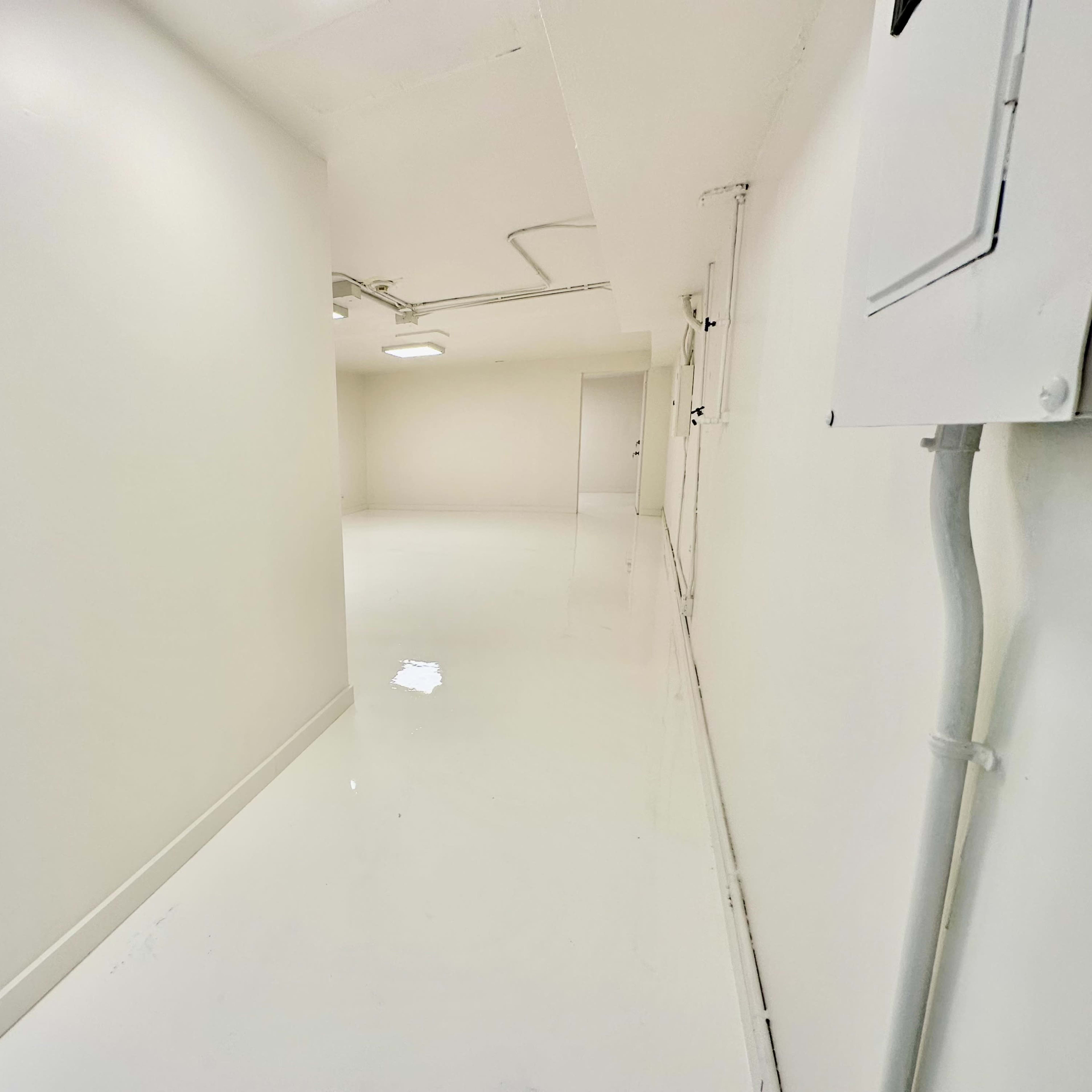 A narrow, well-lit hallway with glossy white walls and a white floor.