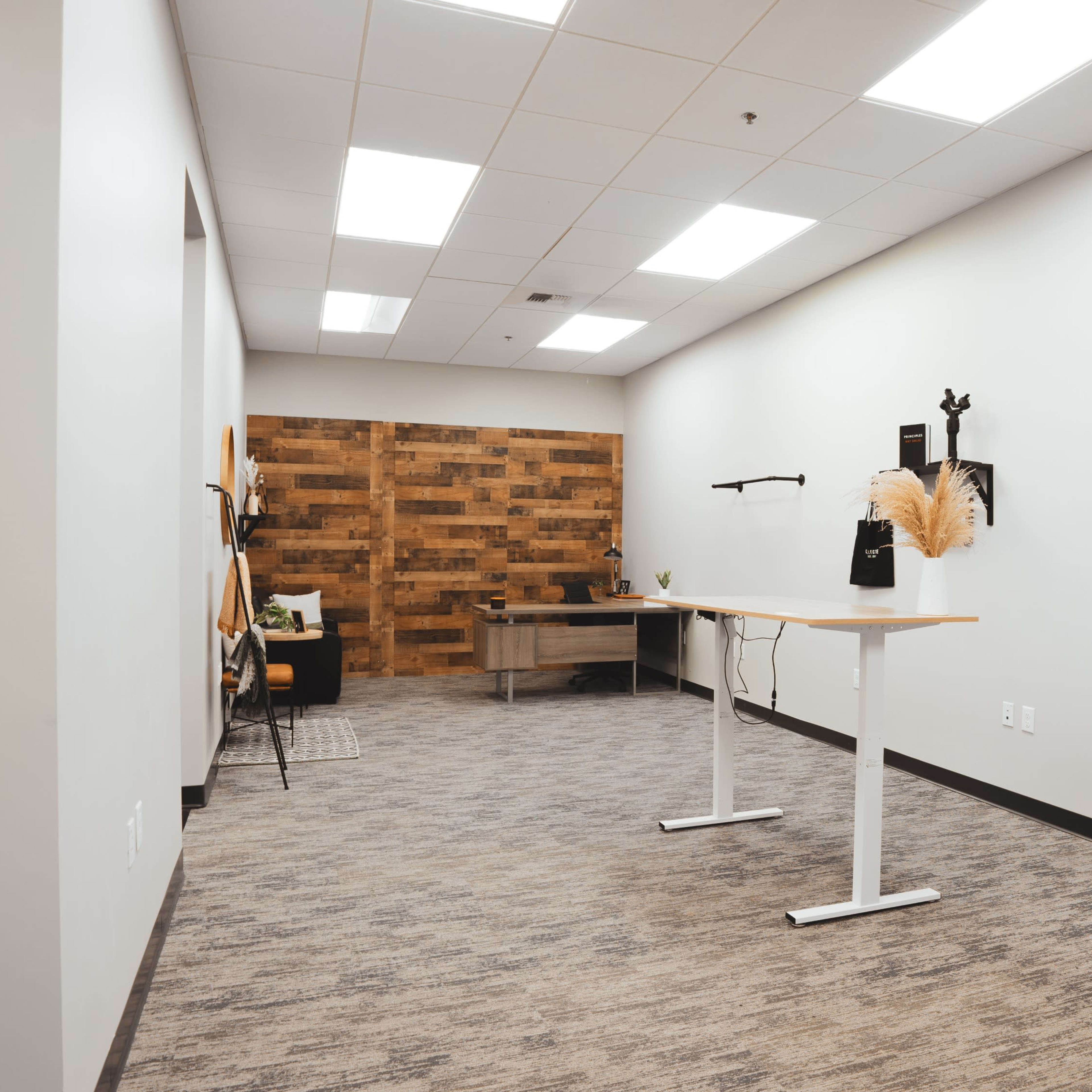 A spacious, minimally furnished office with a standing desk, wooden accent wall, and a few decorative items.