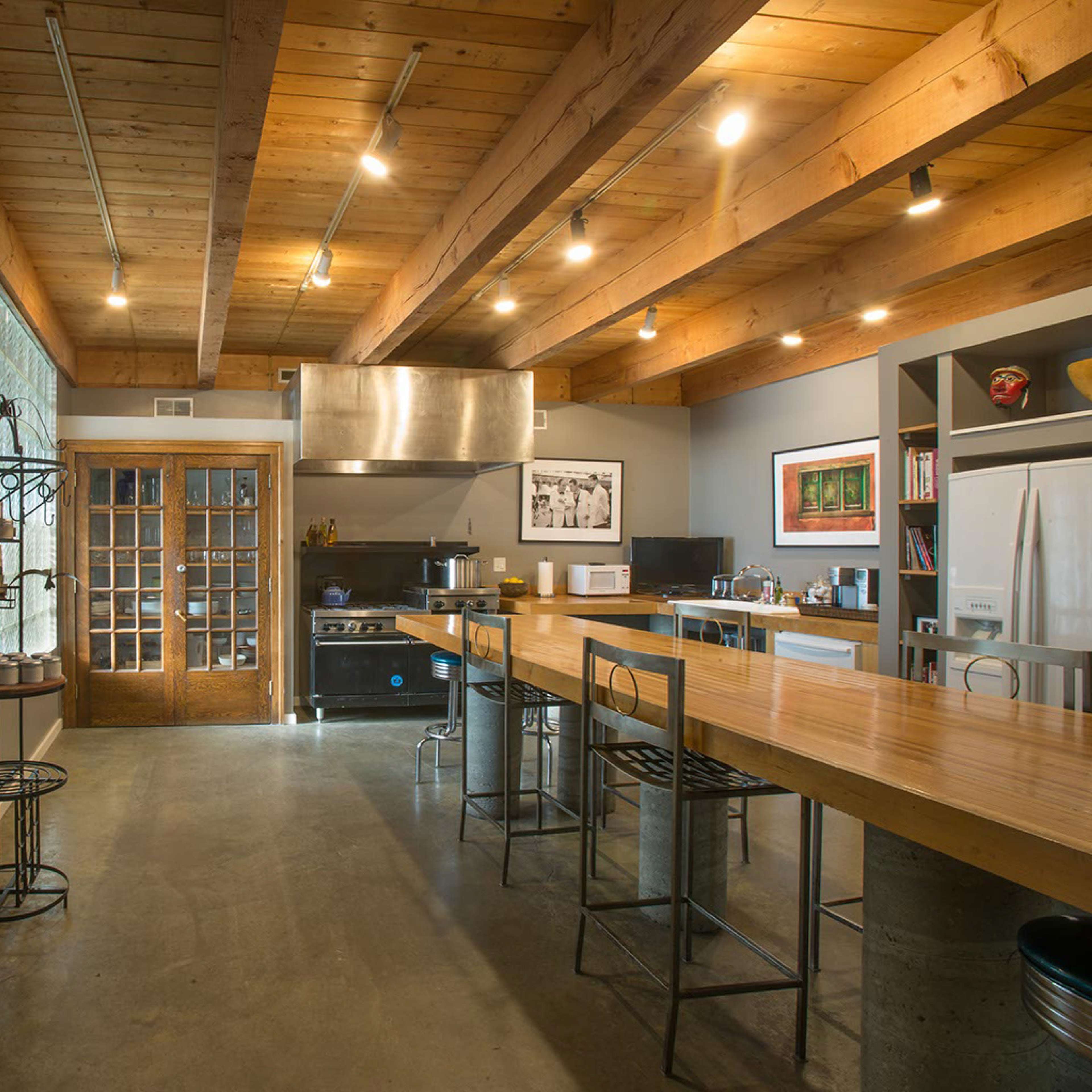 A spacious, modern kitchen with wooden beams, stainless steel appliances, and a large central table.