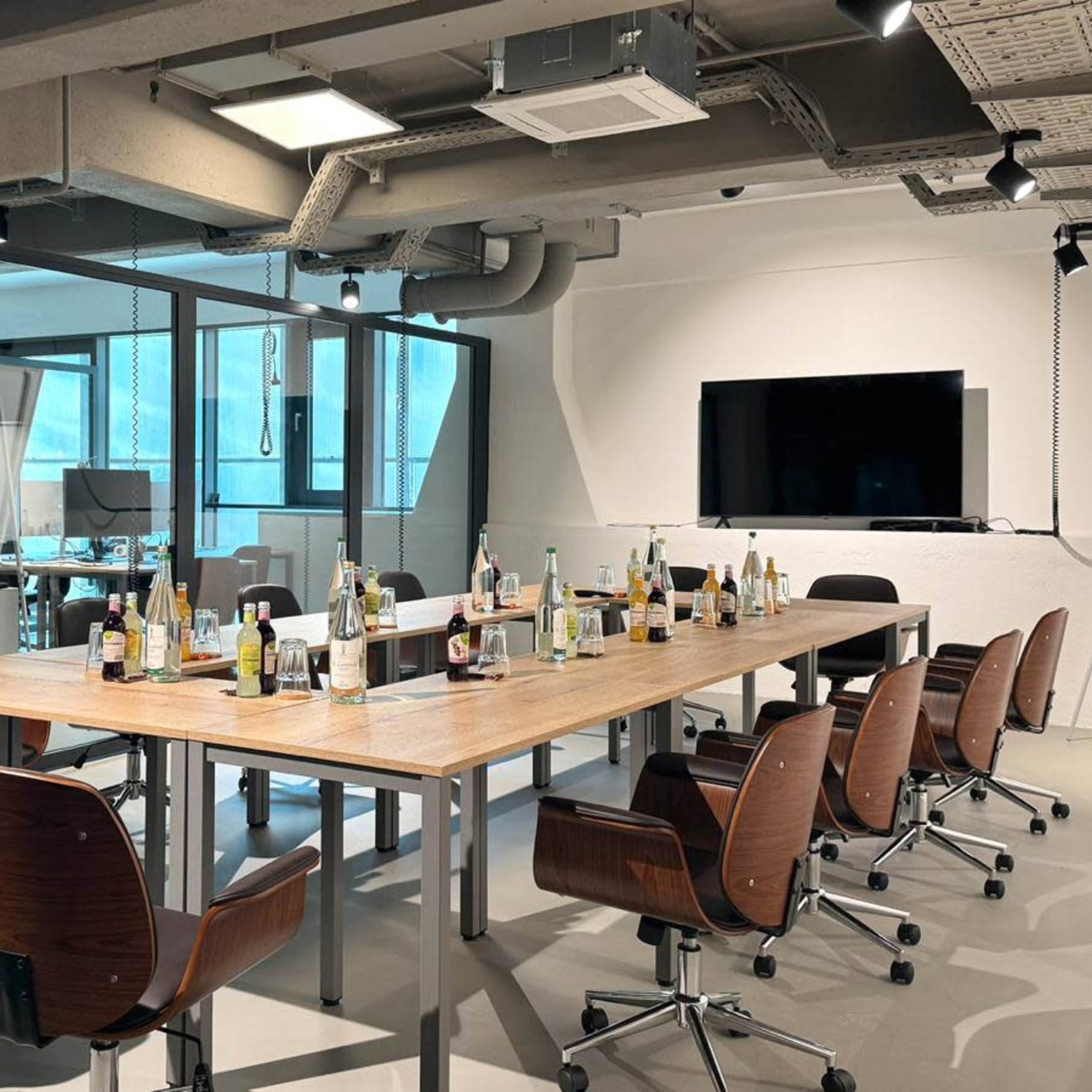 A conference room with a large table surrounded by chairs, featuring empty bottles and a presentation screen on the wall.