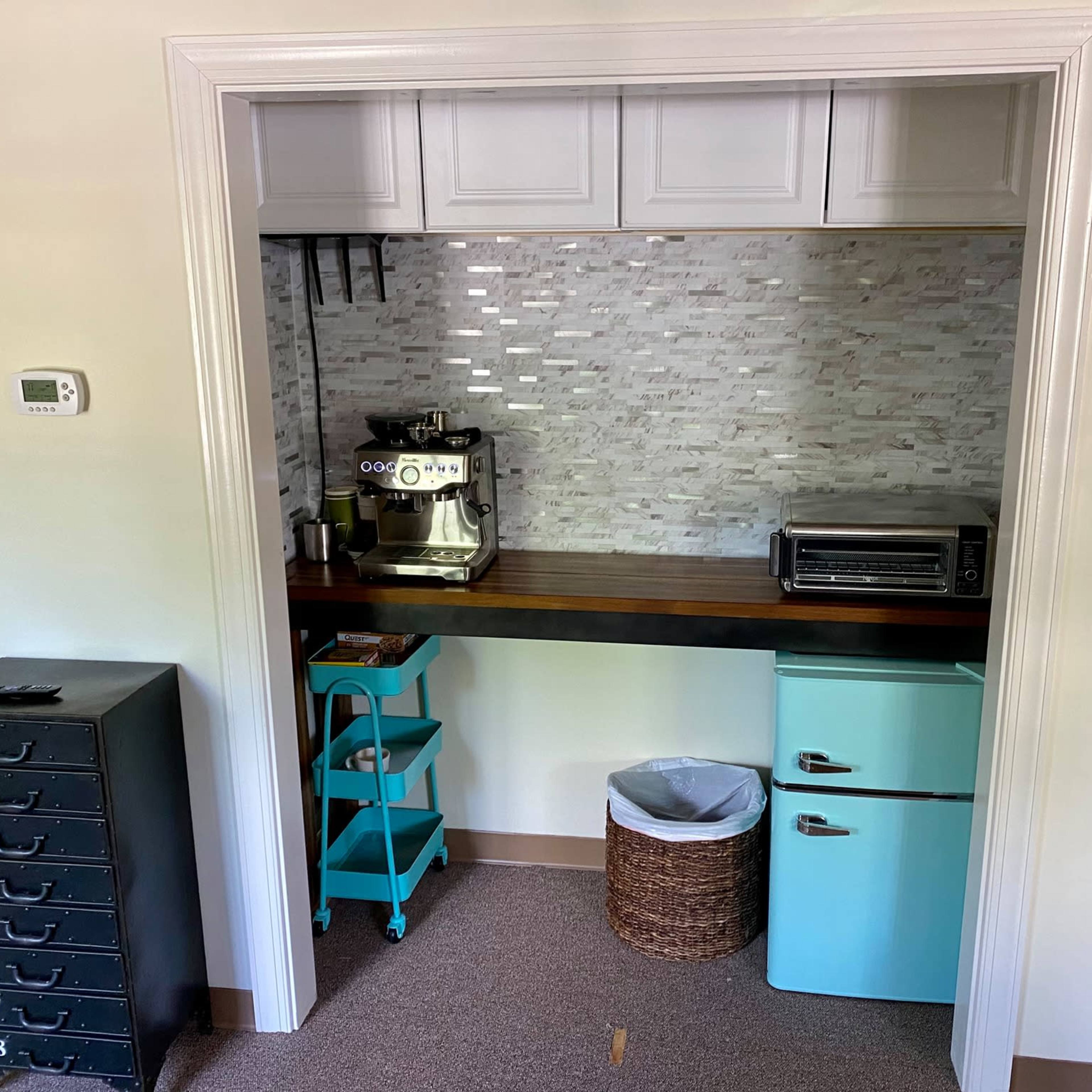 A small kitchen space featuring a coffee machine, a toaster oven, a blue mini fridge, and a stack of storage drawers.