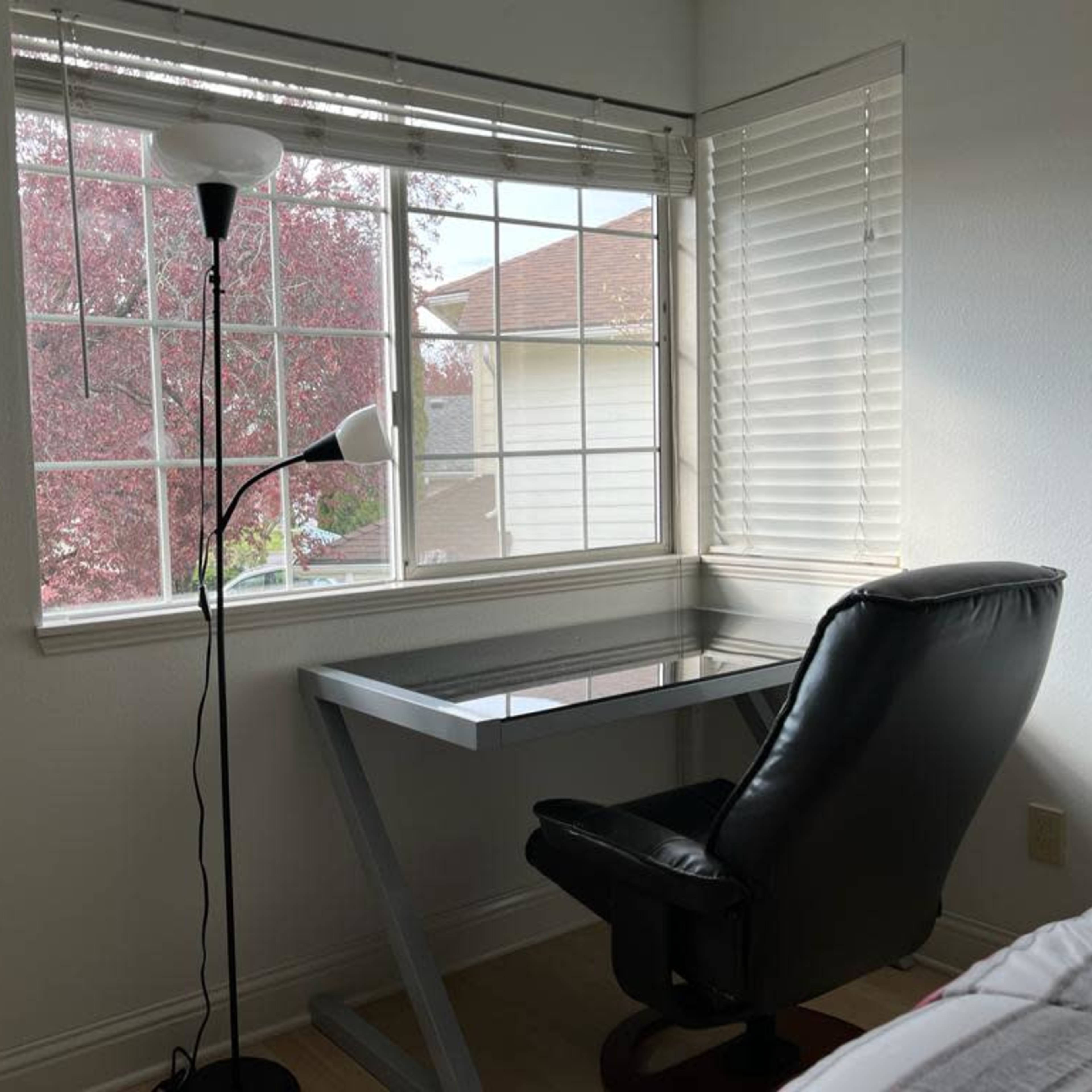 A modern desk with a black chair is positioned by a window overlooking a tree with red leaves.