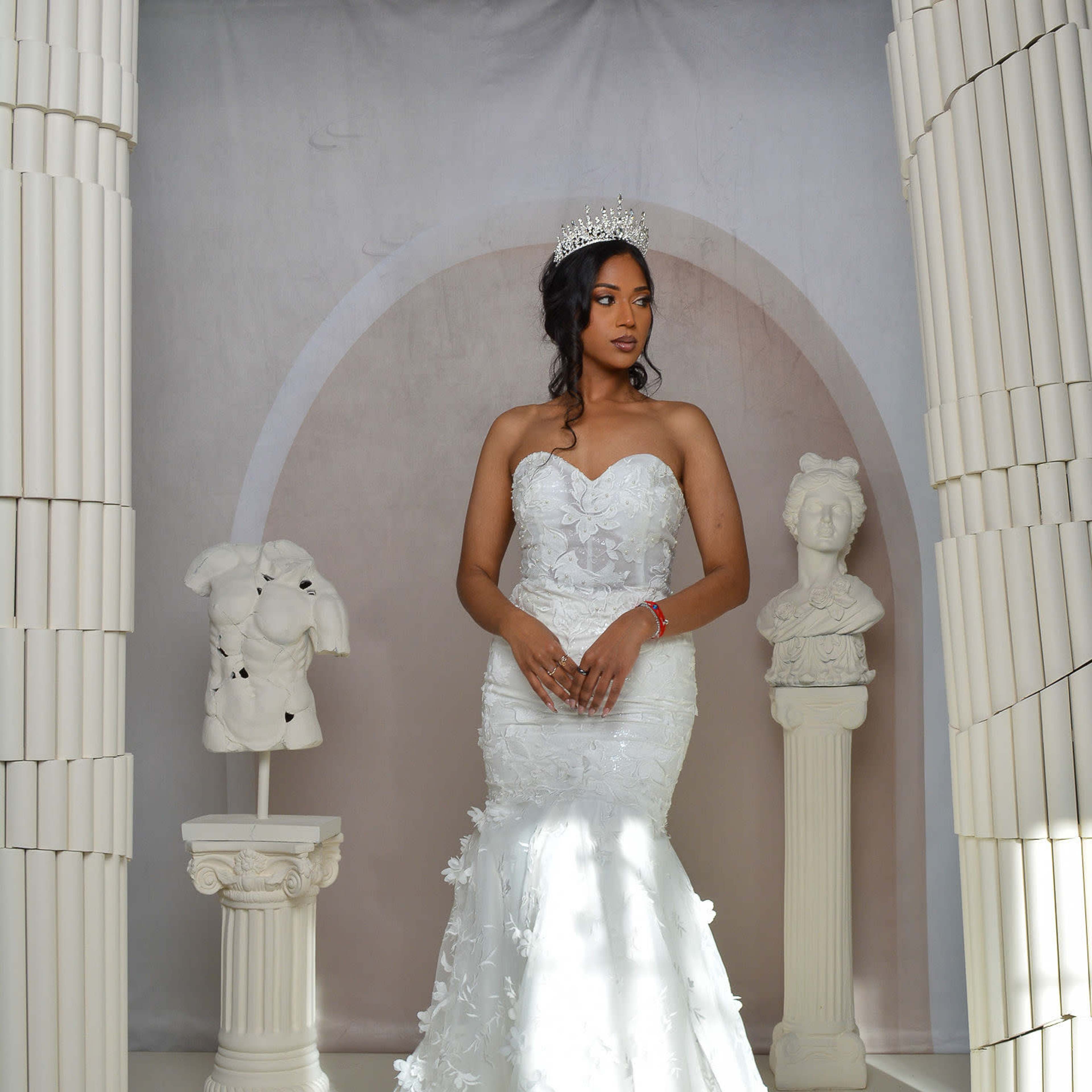 A woman in a white wedding gown stands in front of classical columns and sculptures.