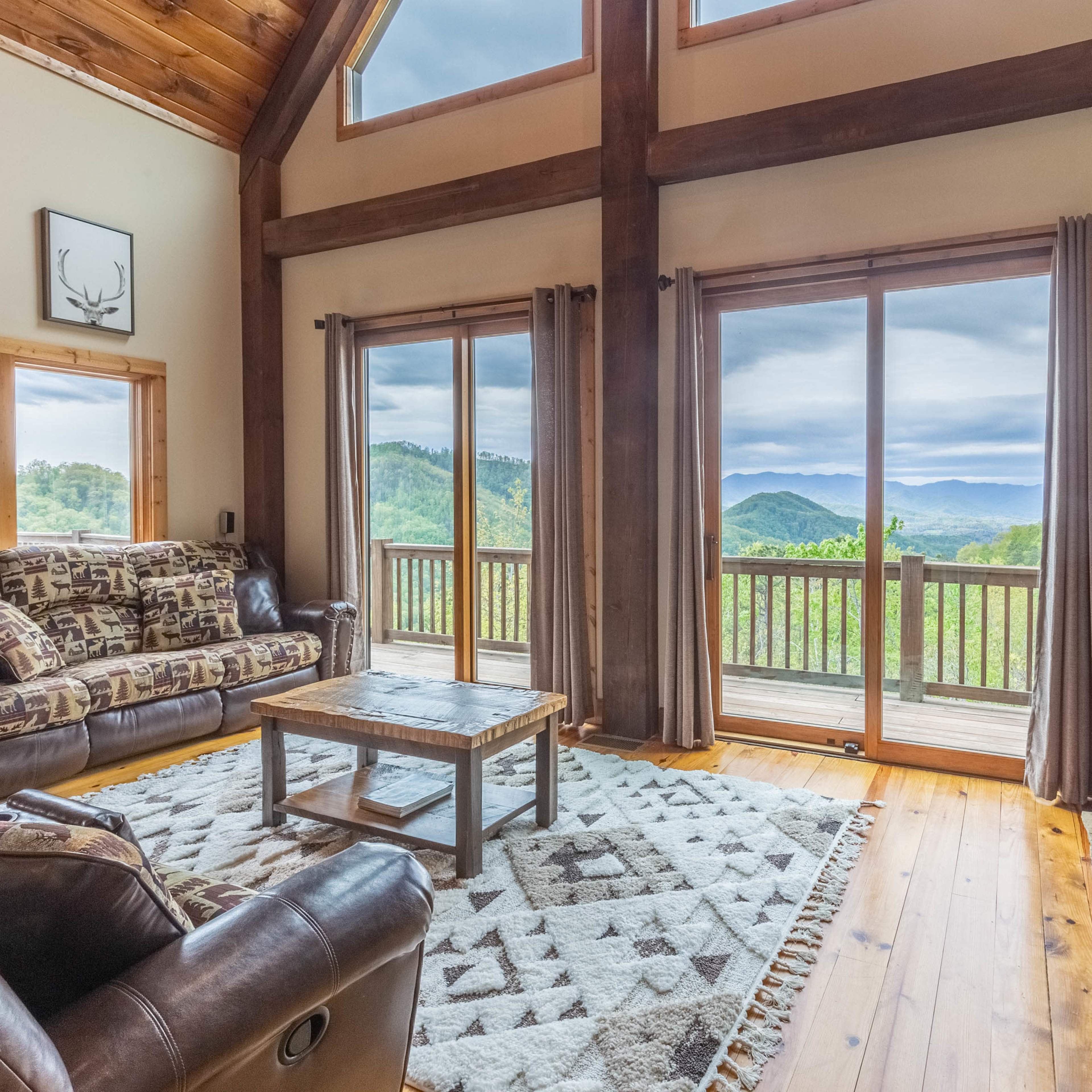 A cozy living room features a stone fireplace and large windows that overlook a mountainous landscape.