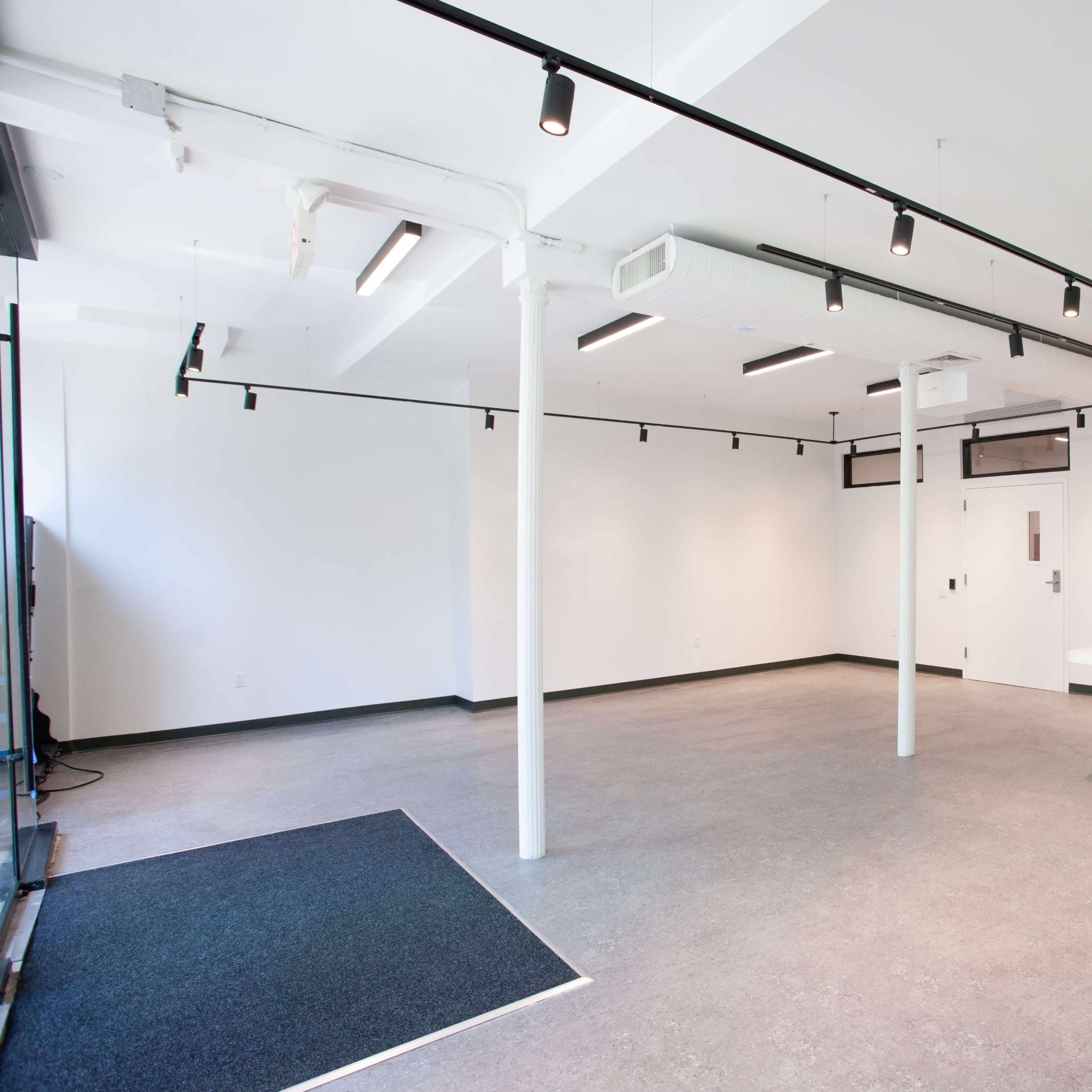 A spacious, empty room with white walls, gray flooring, and recessed lighting.