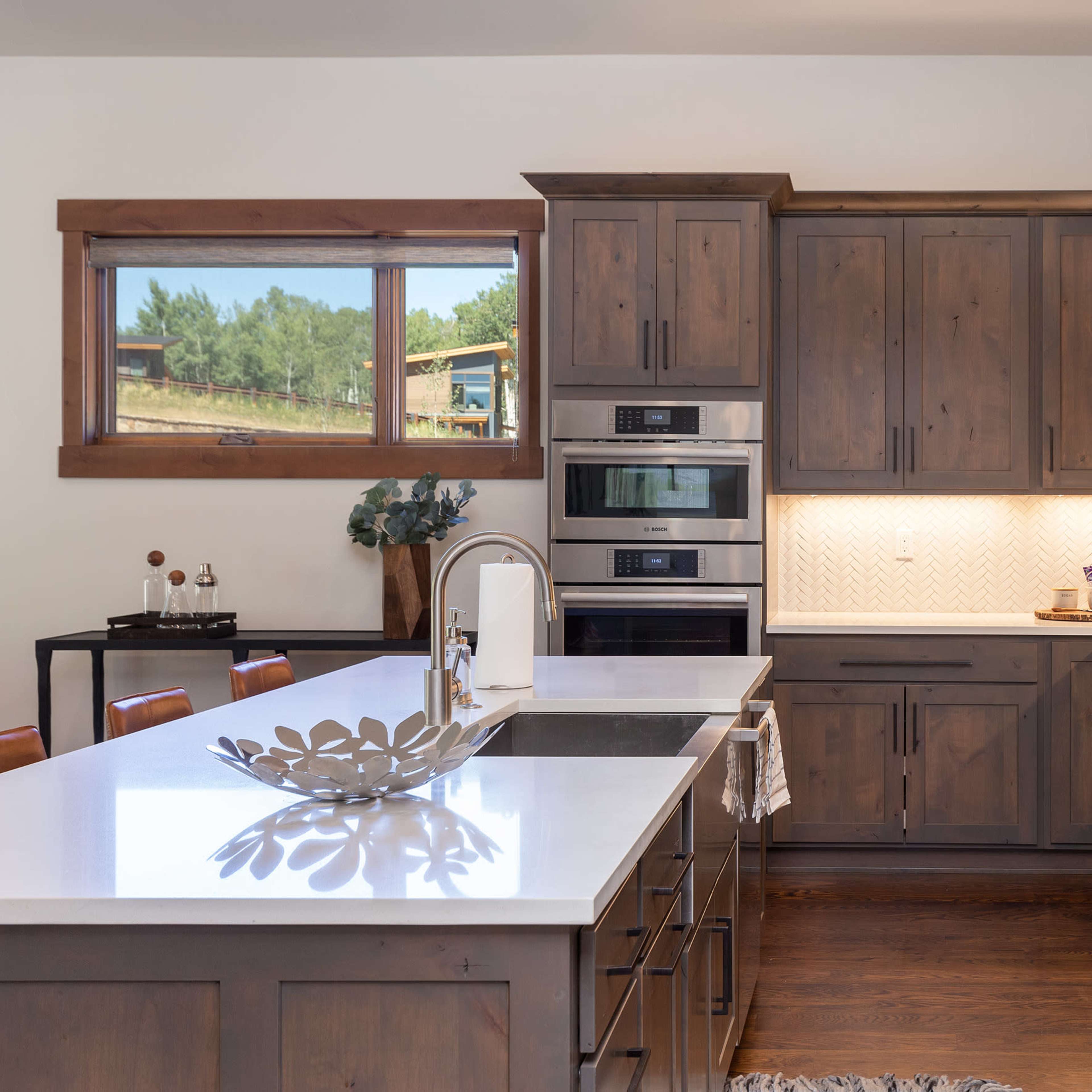 A modern kitchen with wooden cabinets, stainless steel appliances, and a large island topped with a white countertop.