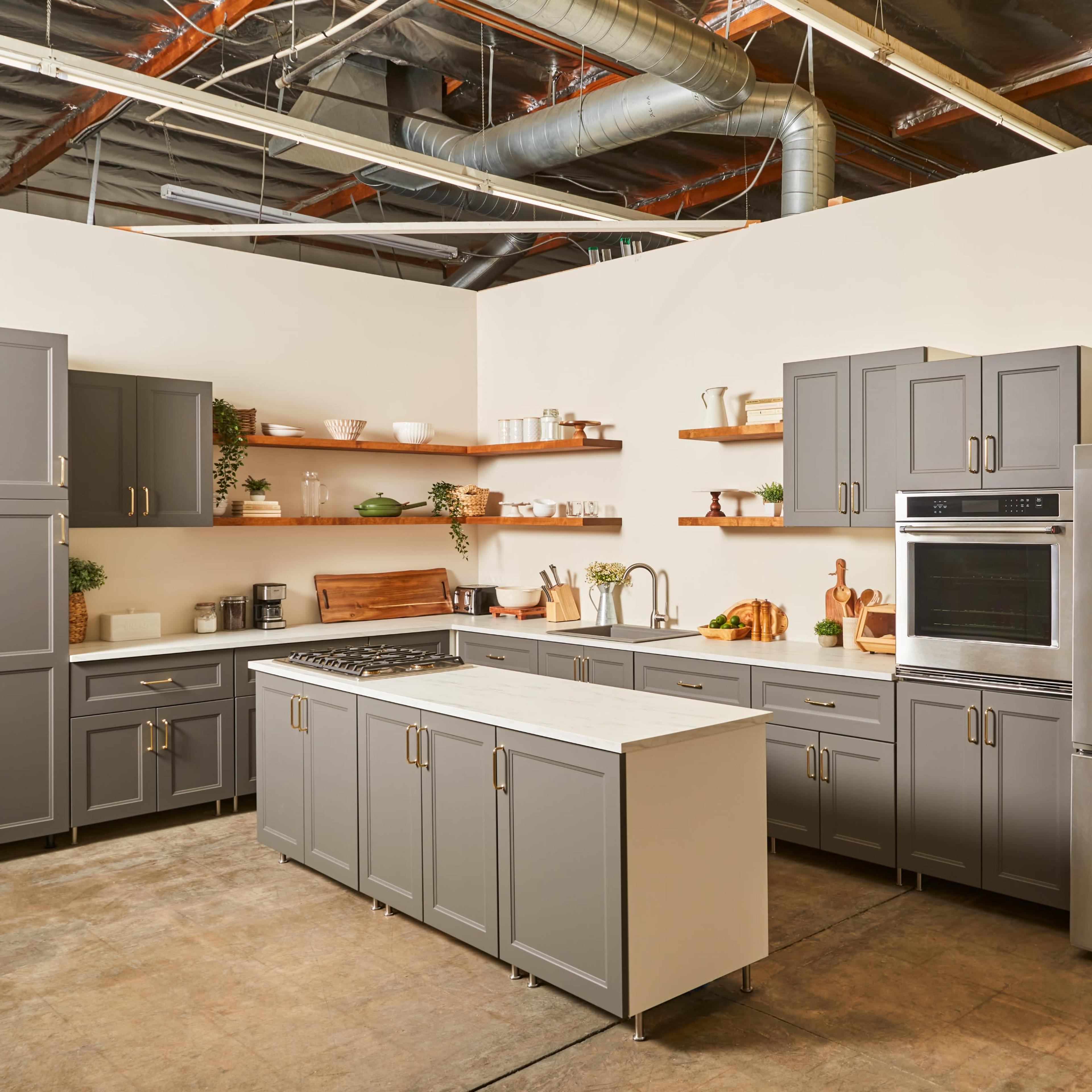 A modern kitchen features gray cabinets, a stainless steel refrigerator, a gas stove, and open shelves displaying various kitchenware.